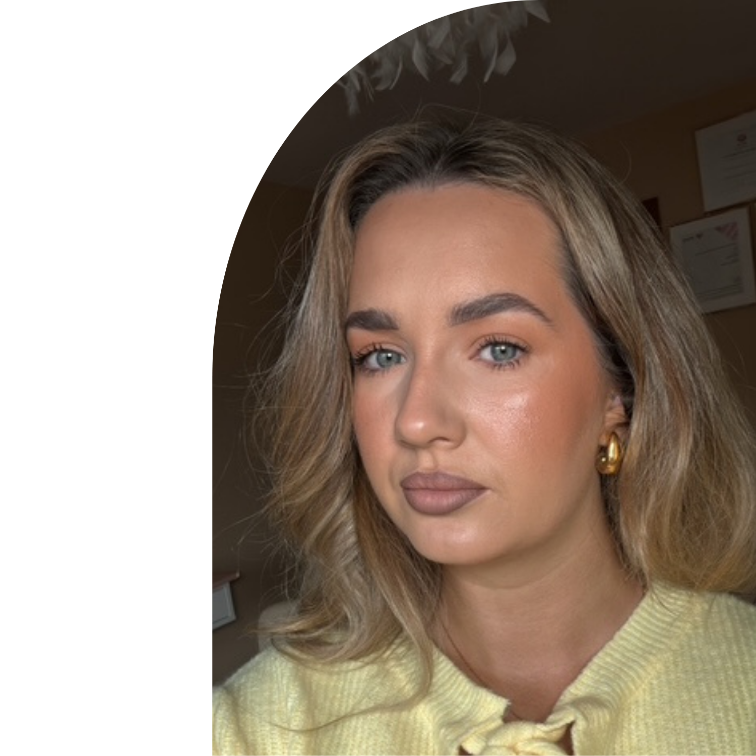 Close-up of a young woman with blonde wavy hair, blue eyes, wearing gold hoop earrings and a yellow sweater. Nicola Manning
