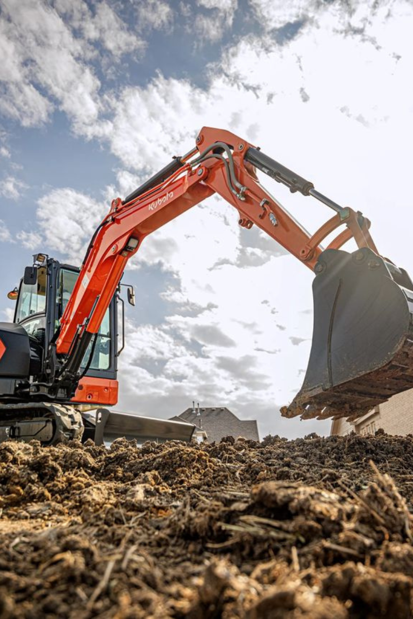 Close-up of an orange Kubota excavator digging into dirt on a cloudy day.