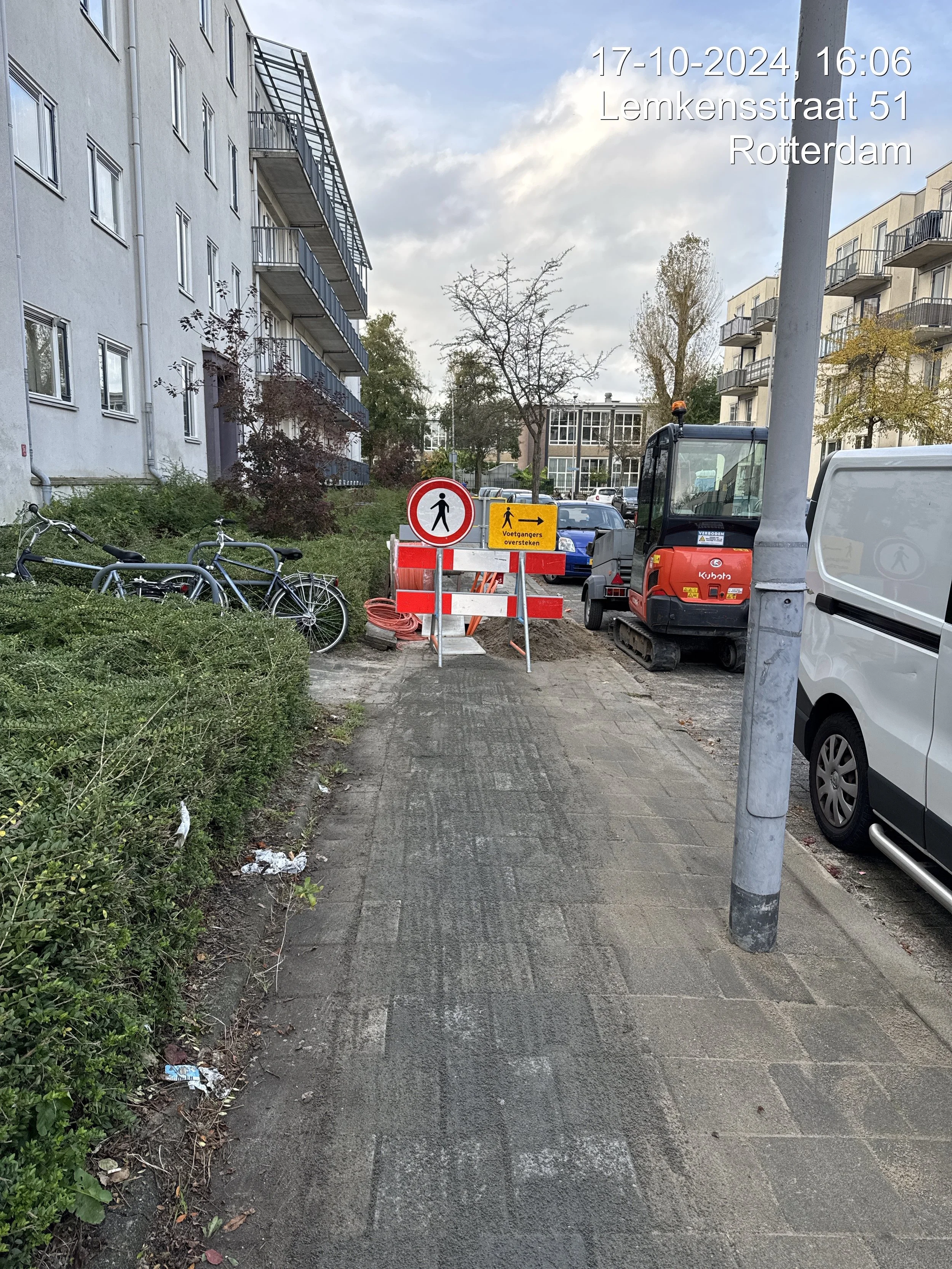 Construction area with warning signs, construction vehicle, parked bikes, and nearby buildings in Rotterdam.