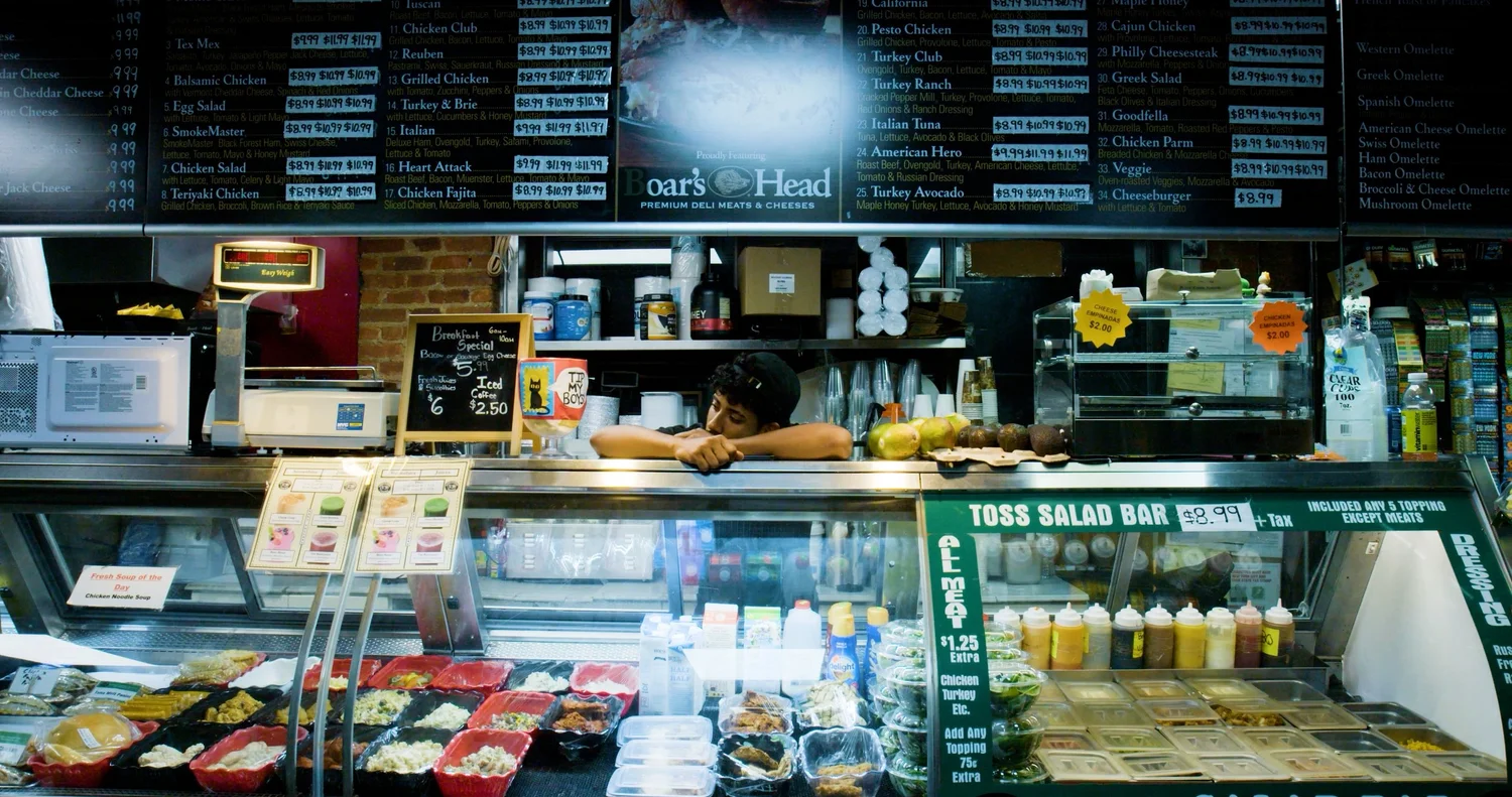 Eugenio rests behind the deli counter beneath the menu boards.