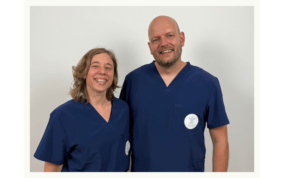 A man and woman wearing blue medical scrubs, smiling, standing against a plain white background.