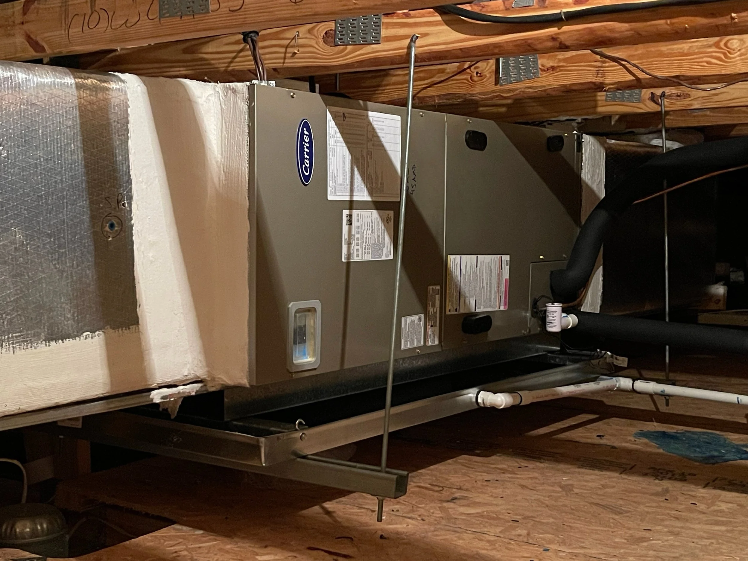 A Carrier HVAC furnace unit installed in an attic space with exposed wooden beams and insulation.