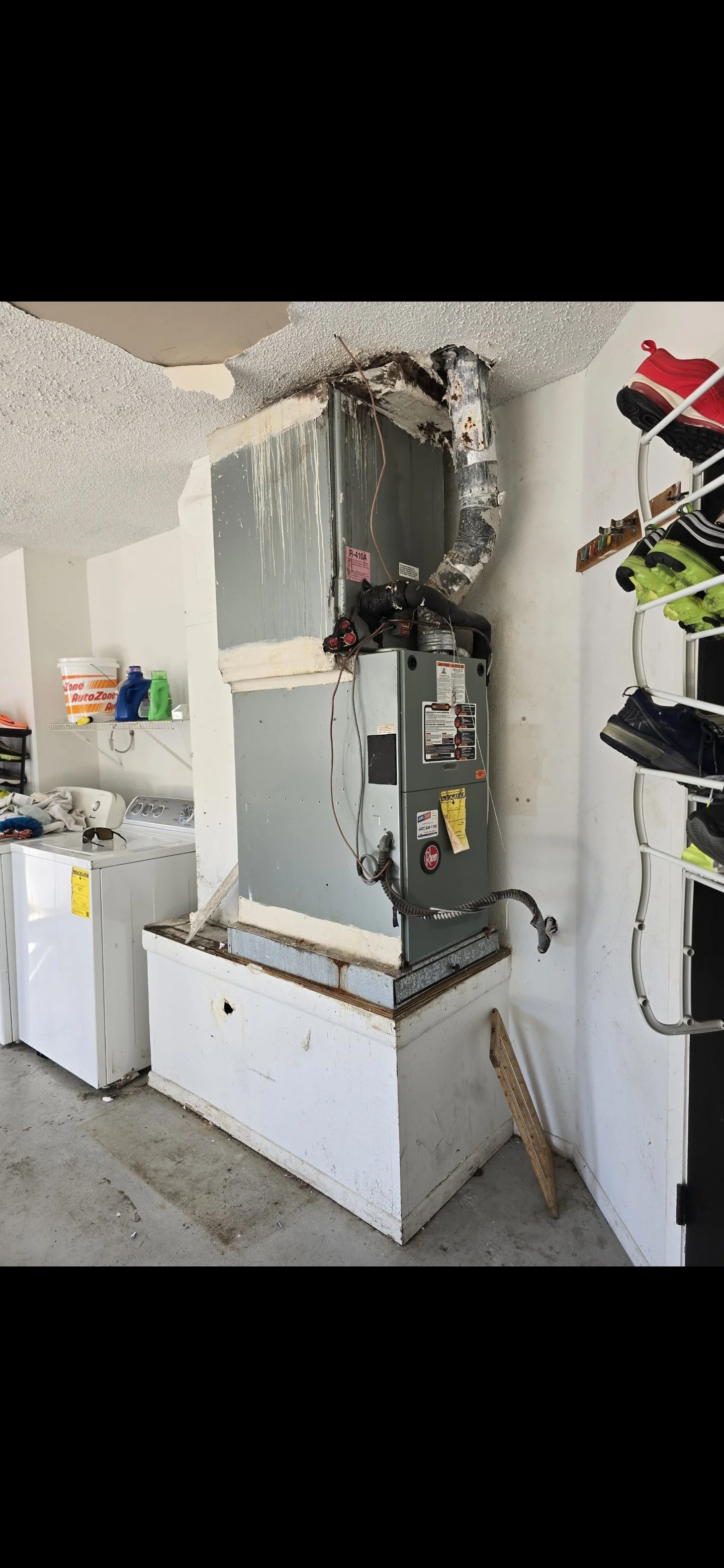 A damaged HVAC unit with charred vents and rust, mounted on a white base in a laundry room. The ceiling above has burned and peeled paint.