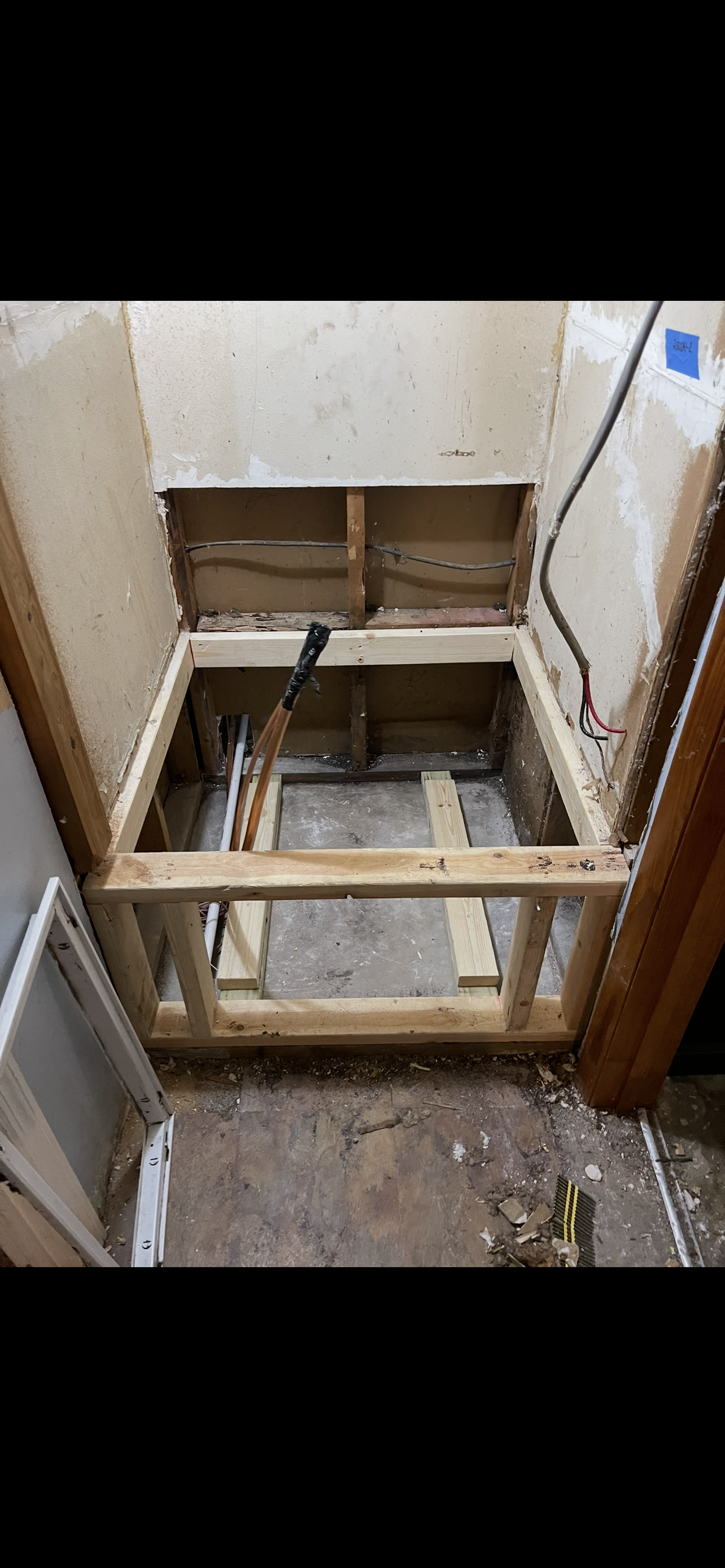 Open bathroom floor showing framing for a new shower or tub area under renovation, with exposed pipes and wall studs.