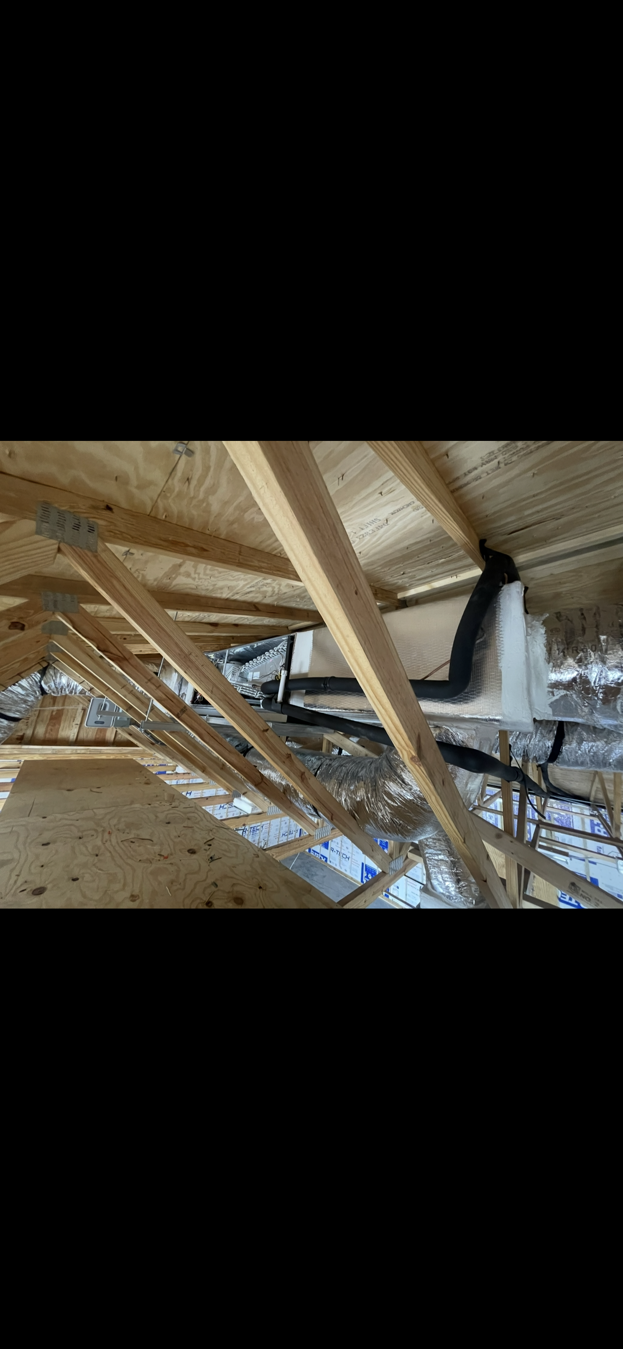 Construction site showing wooden framing, HVAC ductwork, and insulation in an unfinished building.