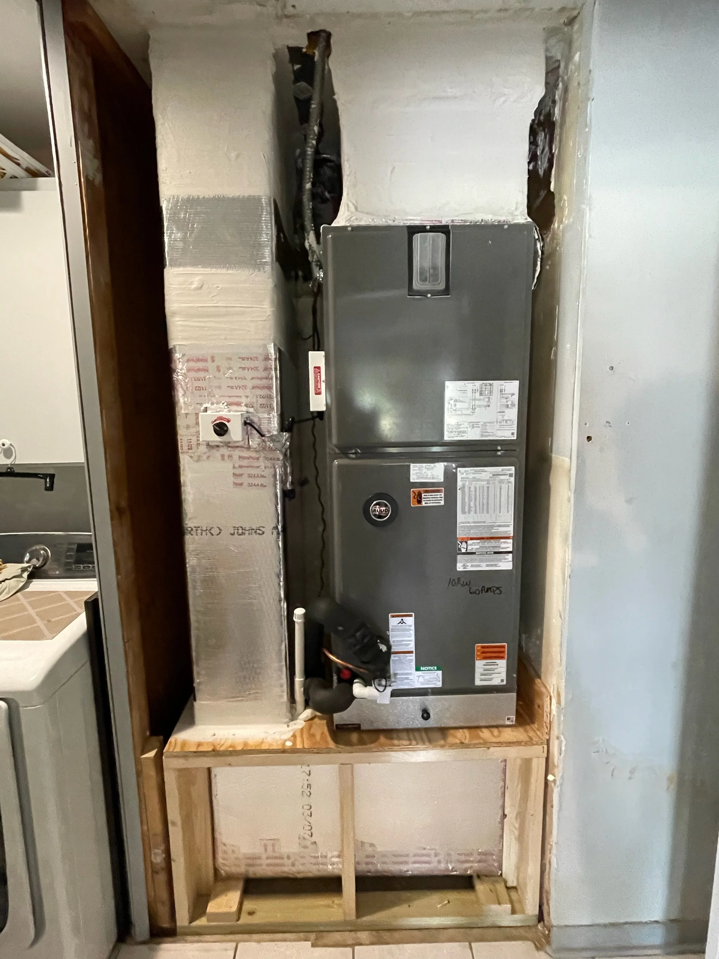 A partially constructed space with exposed drywall framing, insulation, and a large metal HVAC unit installed against the wall.