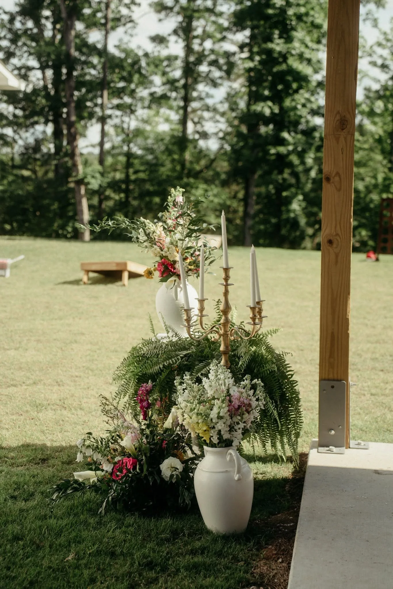 Floral arrangement with candles on a table outdoors, with trees and a bench in the background.