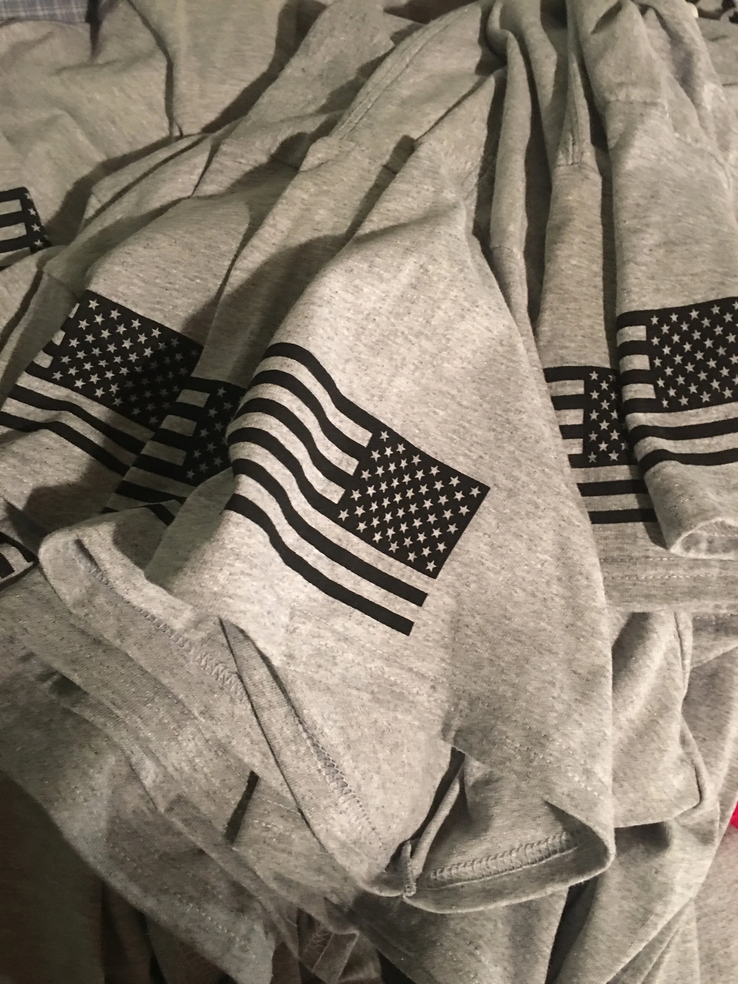 Gray hoodie with a black and white American flag design on the sleeve, rumpled and laid out on a surface.