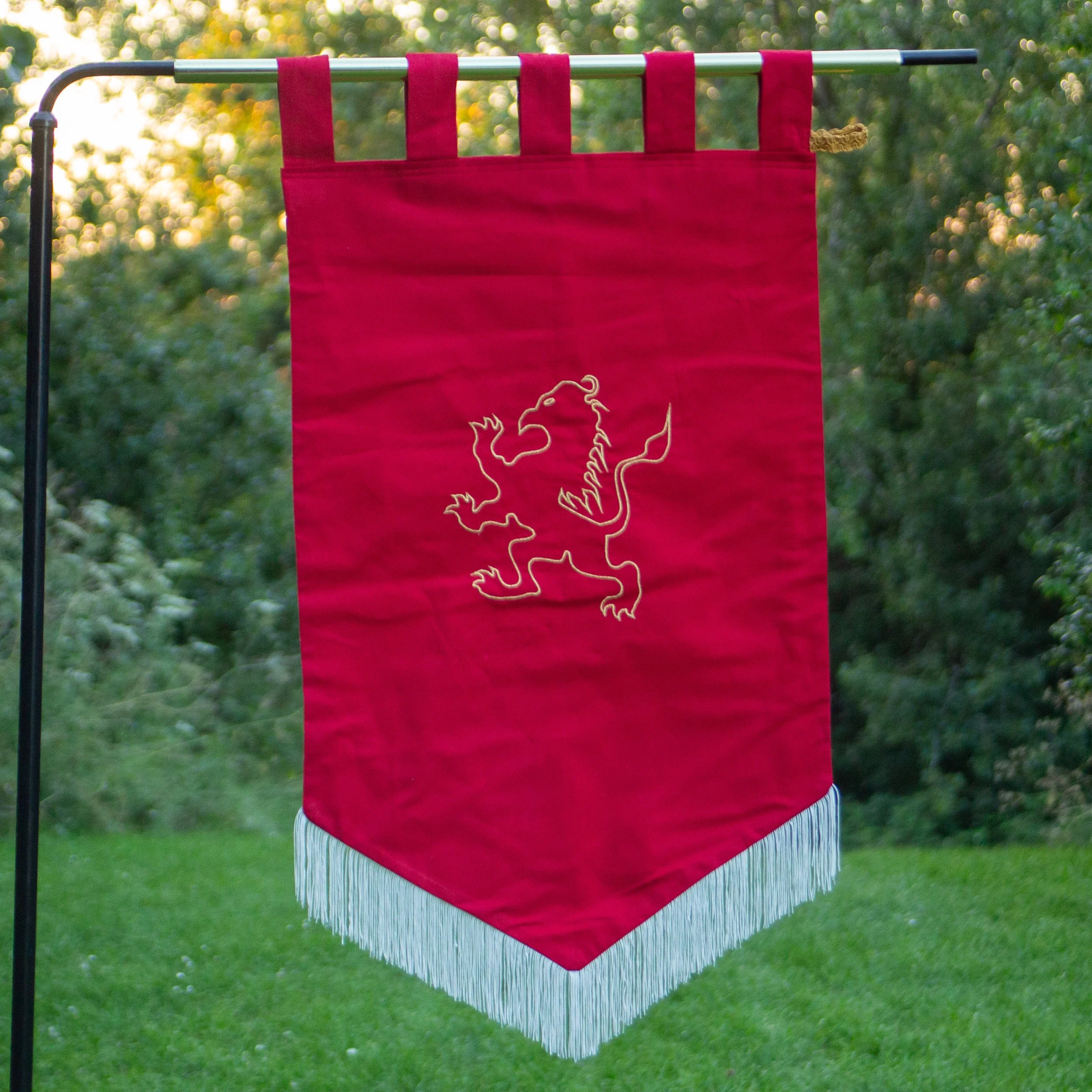 A red banner with a lion outline printed on it, hanging outdoors with trees and sunlight in the background.