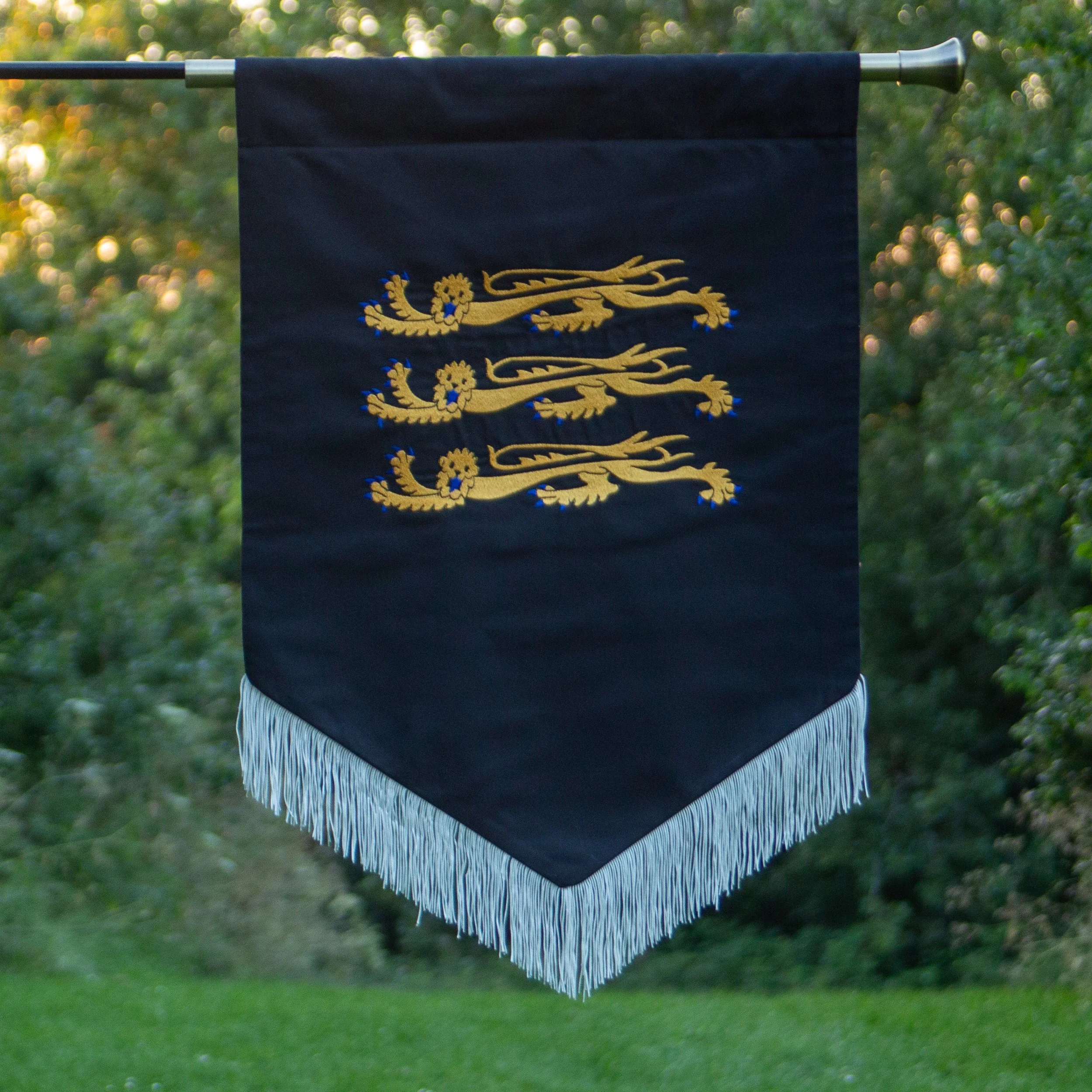 A hanging dark blue banner with three gold embroidered lions and blue accents, outdoors with green blurred trees in the background.