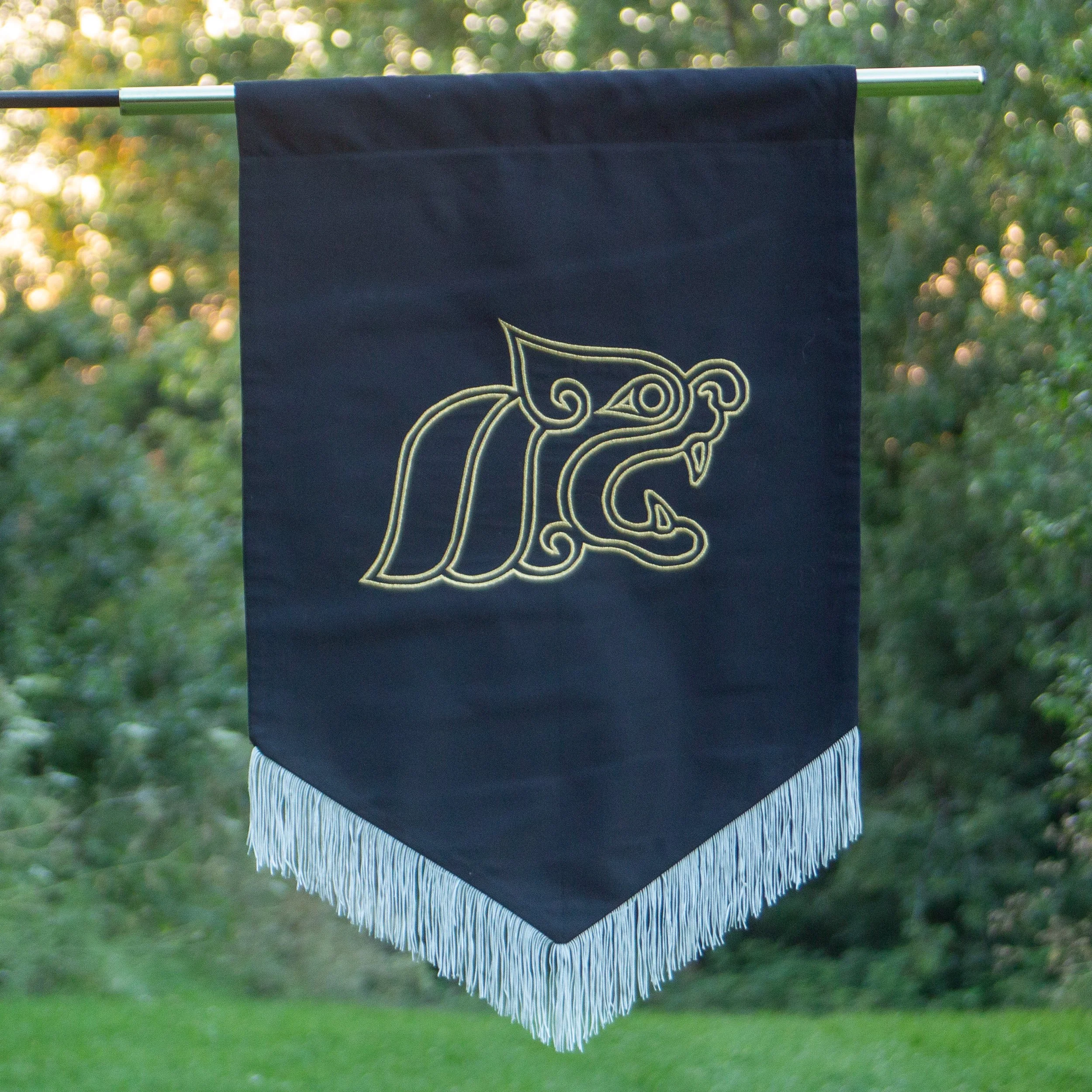 A outdoor flag featuring a medieval lion motif embroidered in gold on a black background,  with trees and sunlight in the background.