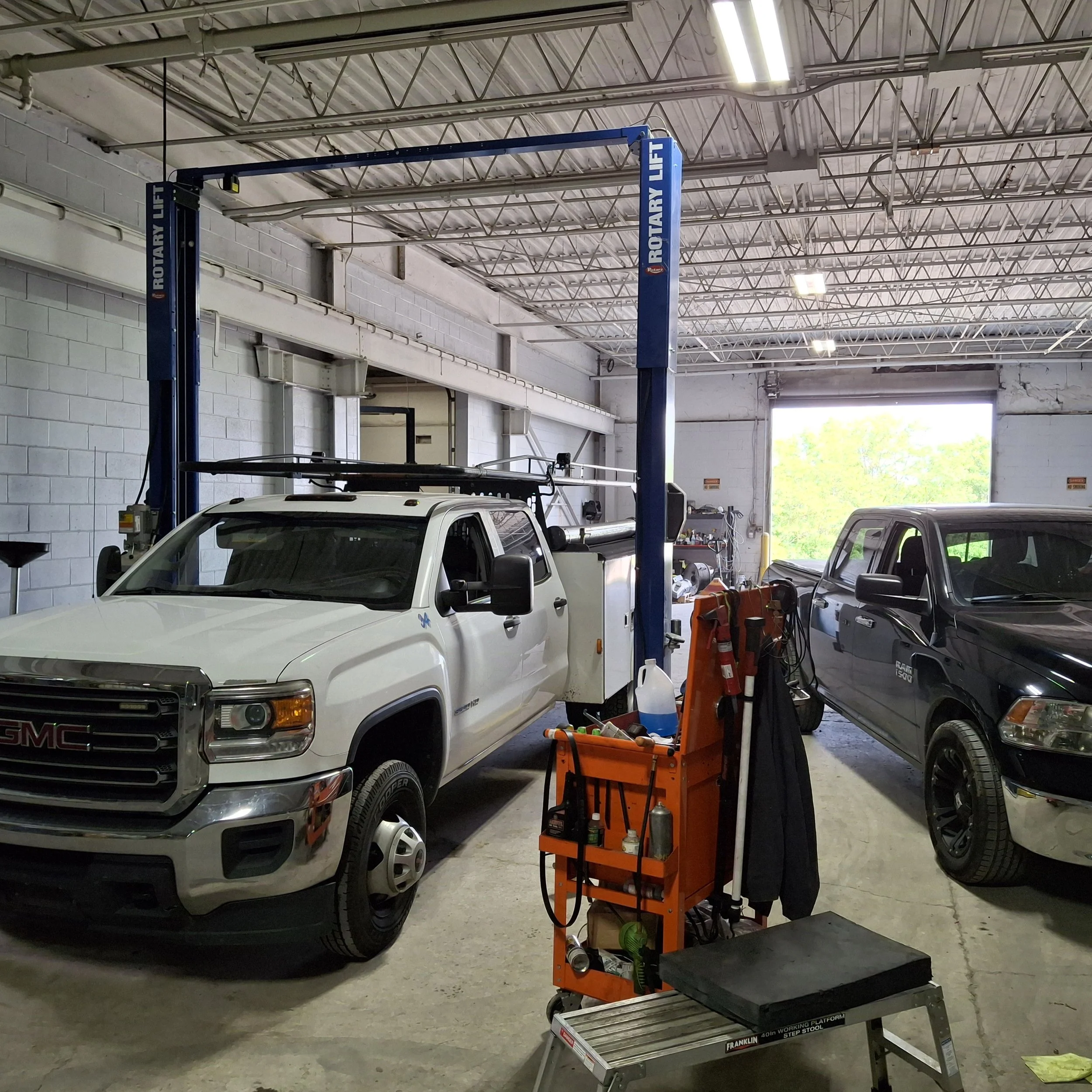 Inside an auto repair garage with a white GMC truck on a lift, various tools, and equipment visible.