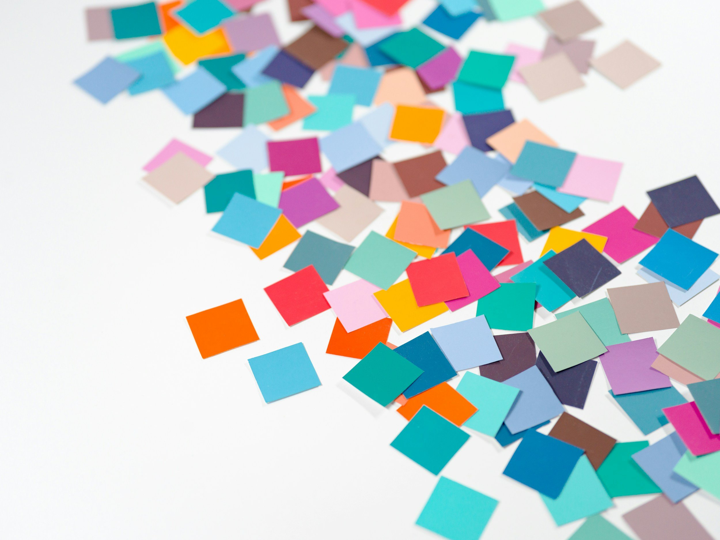 Colorful small paper squares scattered across a white surface.