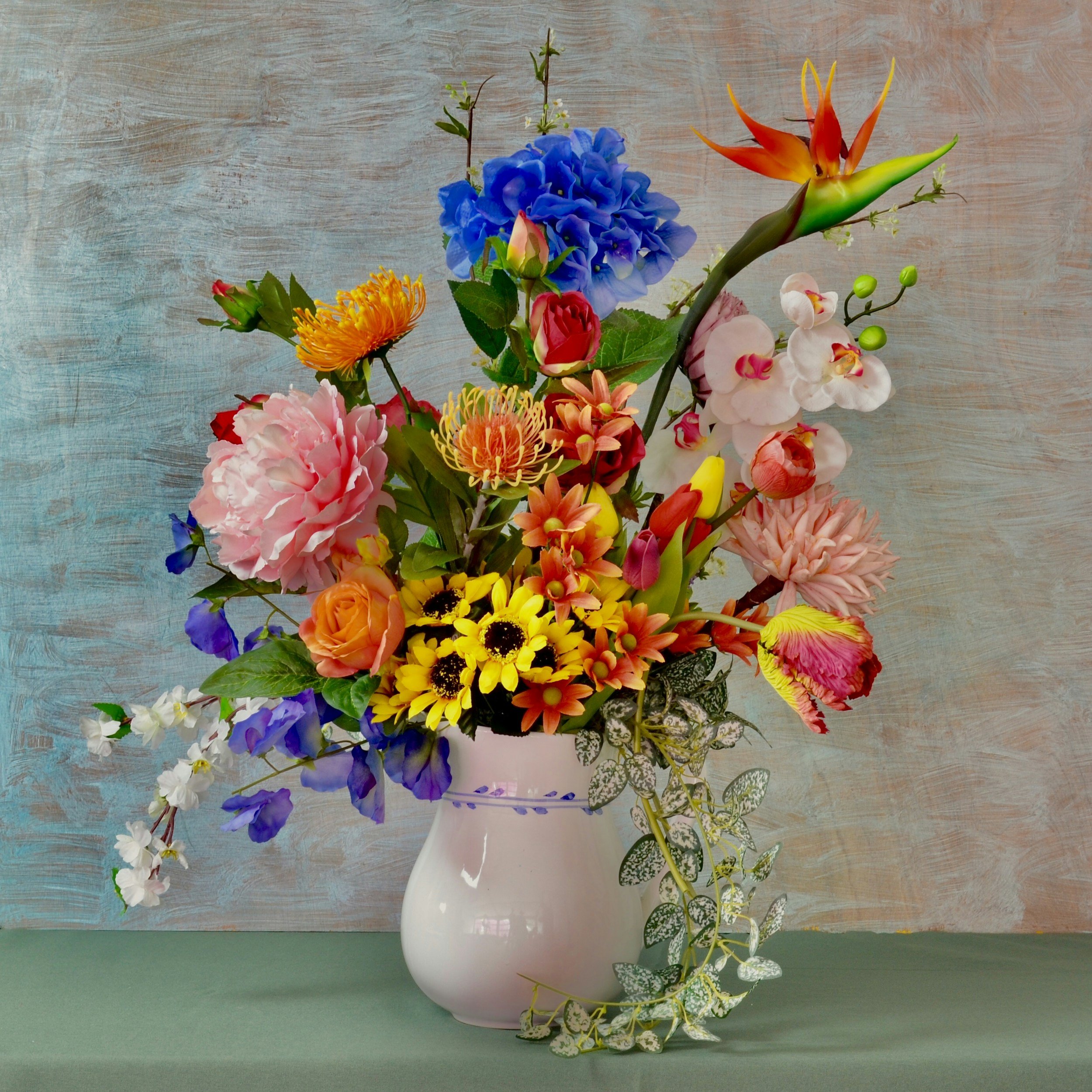 A variety of colorful flowers arranged in a white vase on a two-tone background.