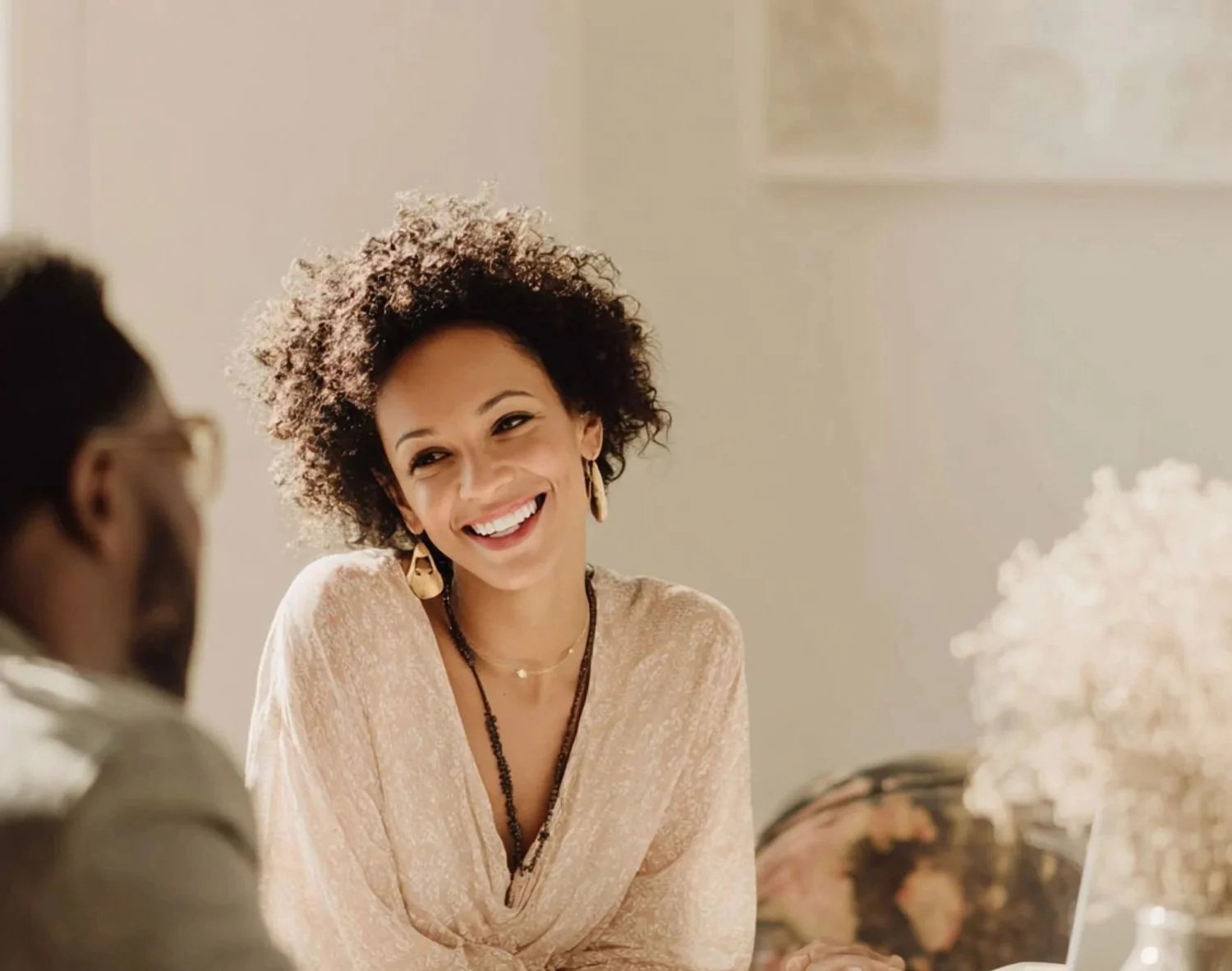 A woman with curly hair smiling and talking to another person in a well-lit room.