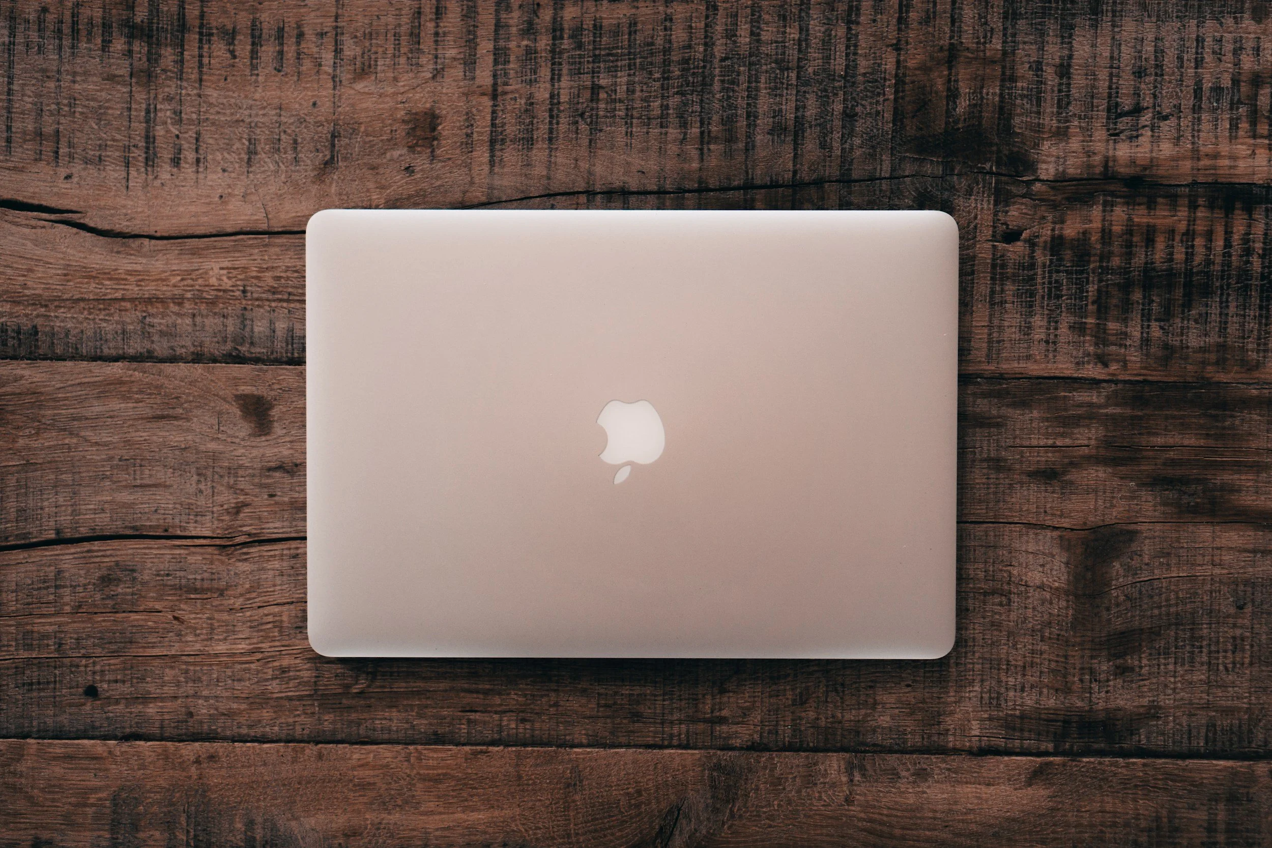 Top view of closed silver Apple MacBook matching the rustic wooden table background.