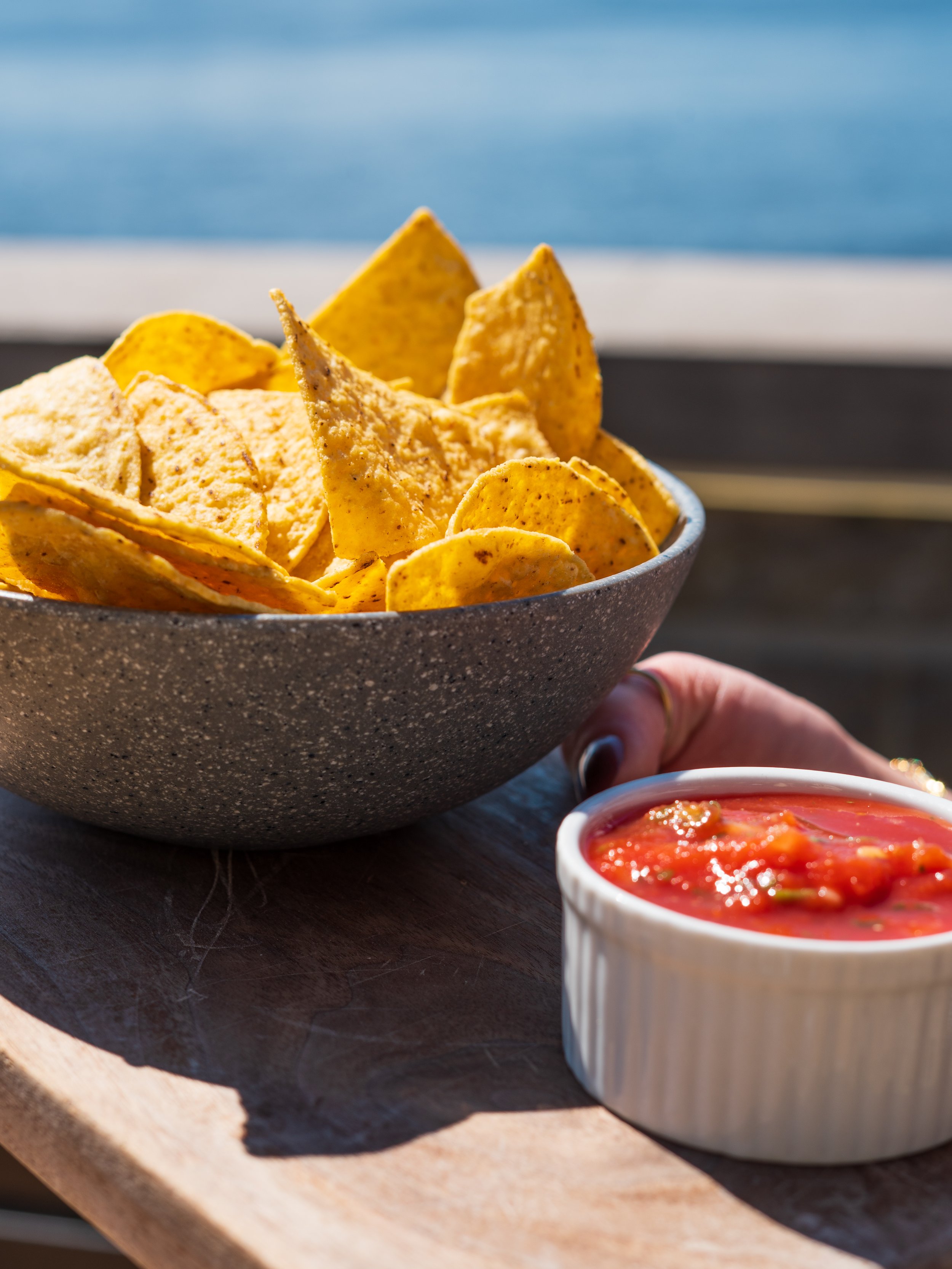 A bowl of tortilla chips with a small cup of salsa on a wooden surface.