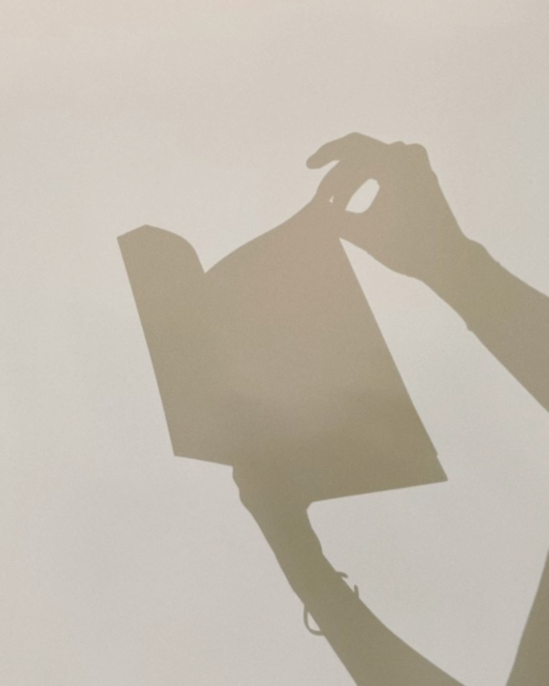 Silhouette of a hand holding a smartphone, casting a shadow on a wall.