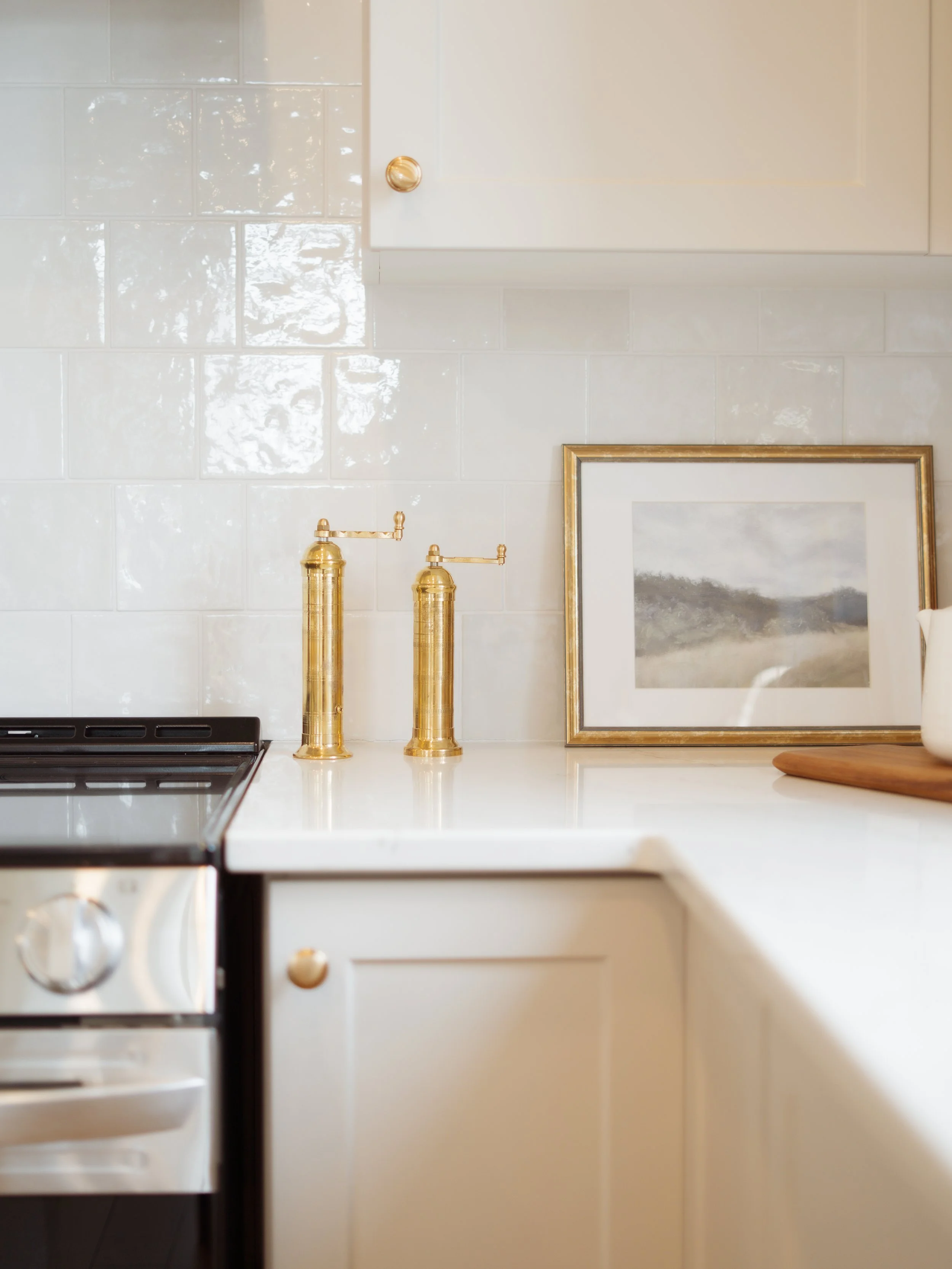 A kitchen countertop with two gold soap dispensers, a framed picture of a landscape, and part of a stovetop visible.