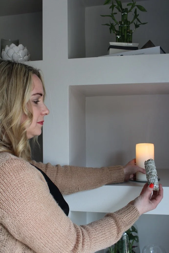 Holistic therapist lighting a candle on a shelf in a calm, softly lit wellbeing space