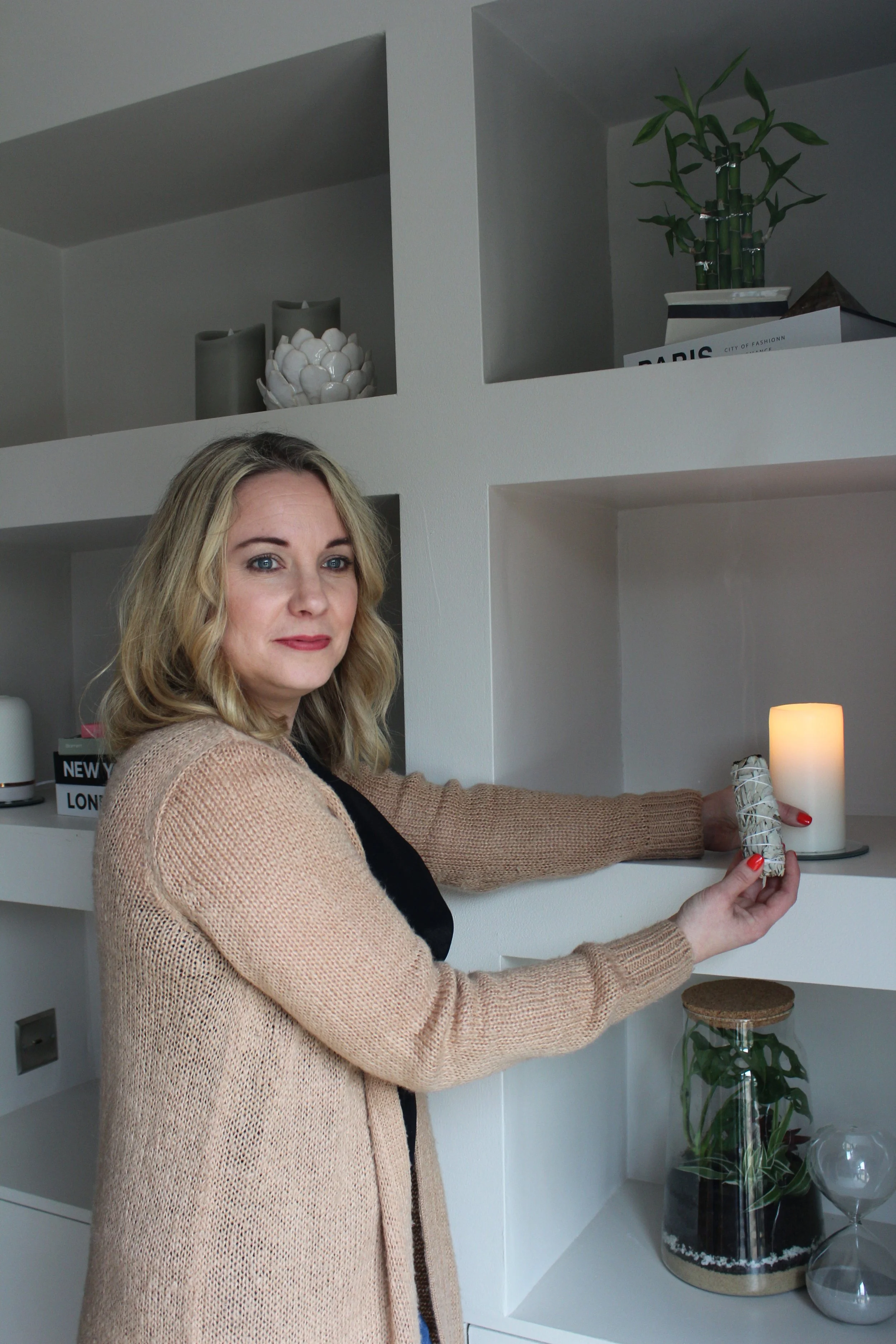 Holistic therapist lighting a candle on a shelf in a calm, softly lit wellbeing space