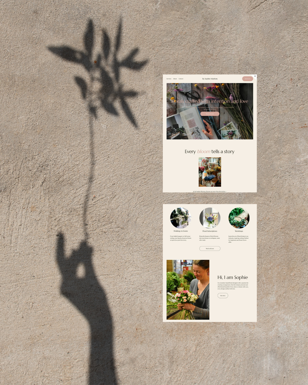 A computer screen displaying a website for a floral business on a sandy surface, with a shadow of a hand holding a small plant or flower cast nearby.