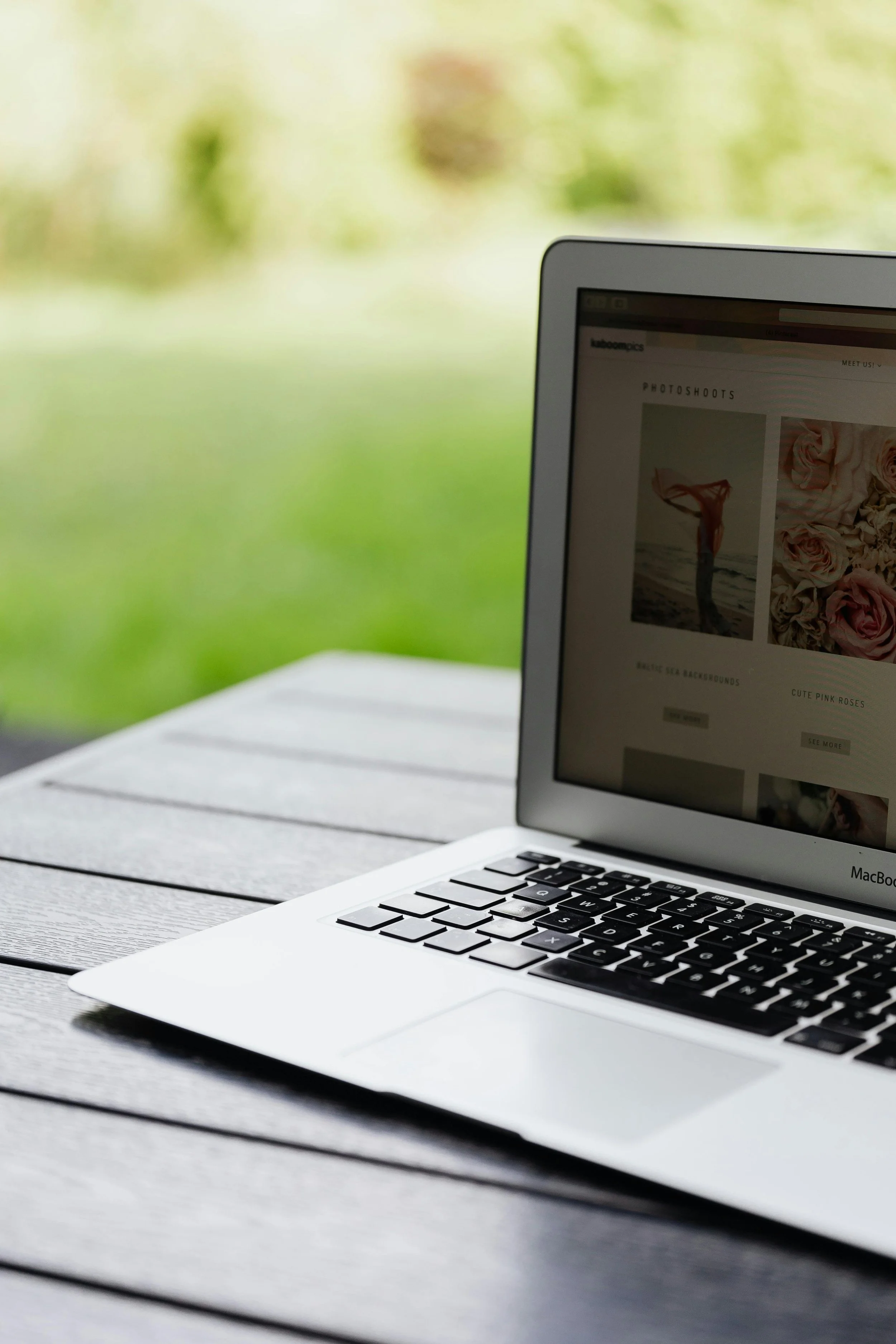 Open MacBook laptop on a wooden outdoor table with a blurred green natural background.