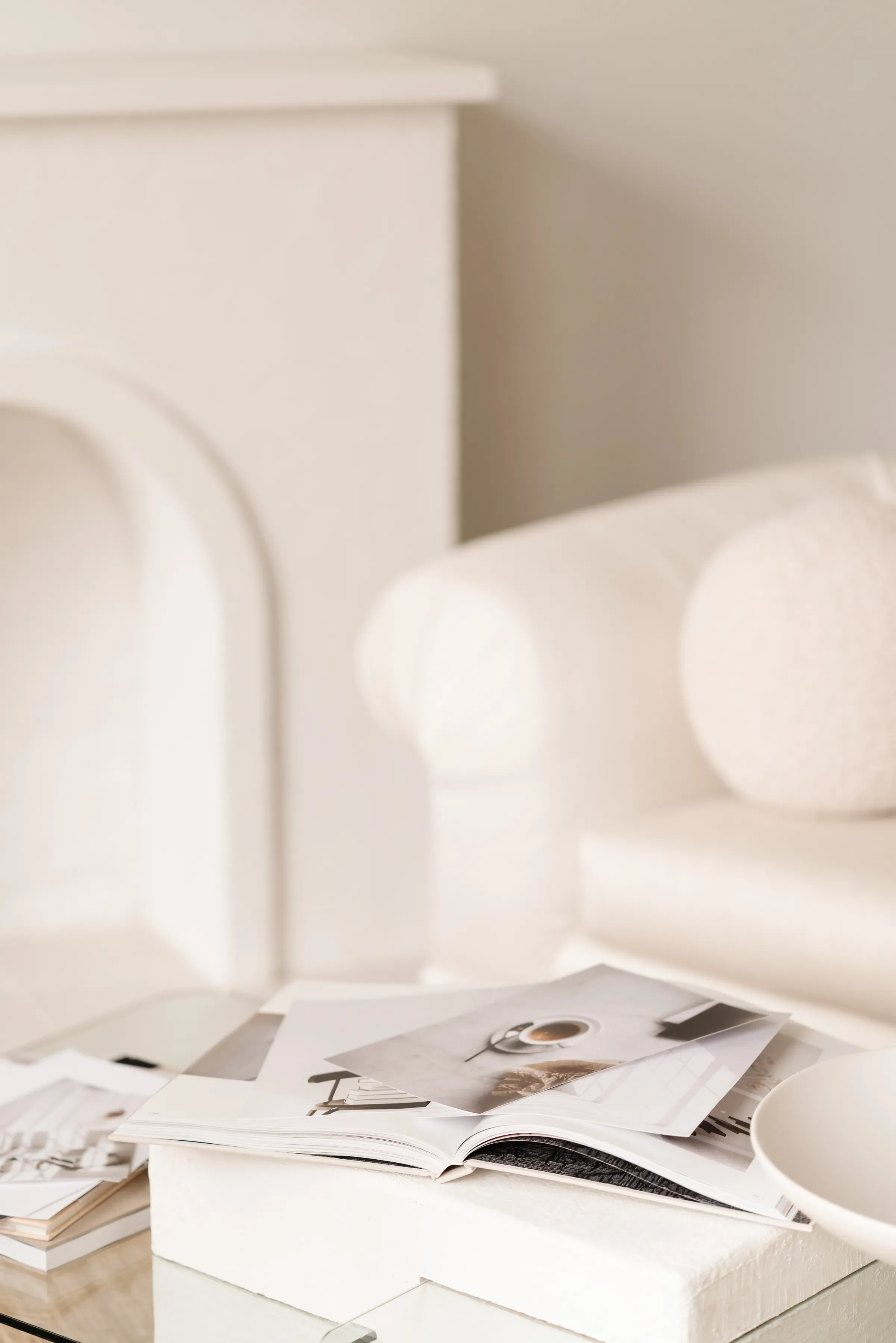 Open magazine with fashion photos lying on a white surface, next to a white cup, with more magazines stacked nearby in a minimalist setting.