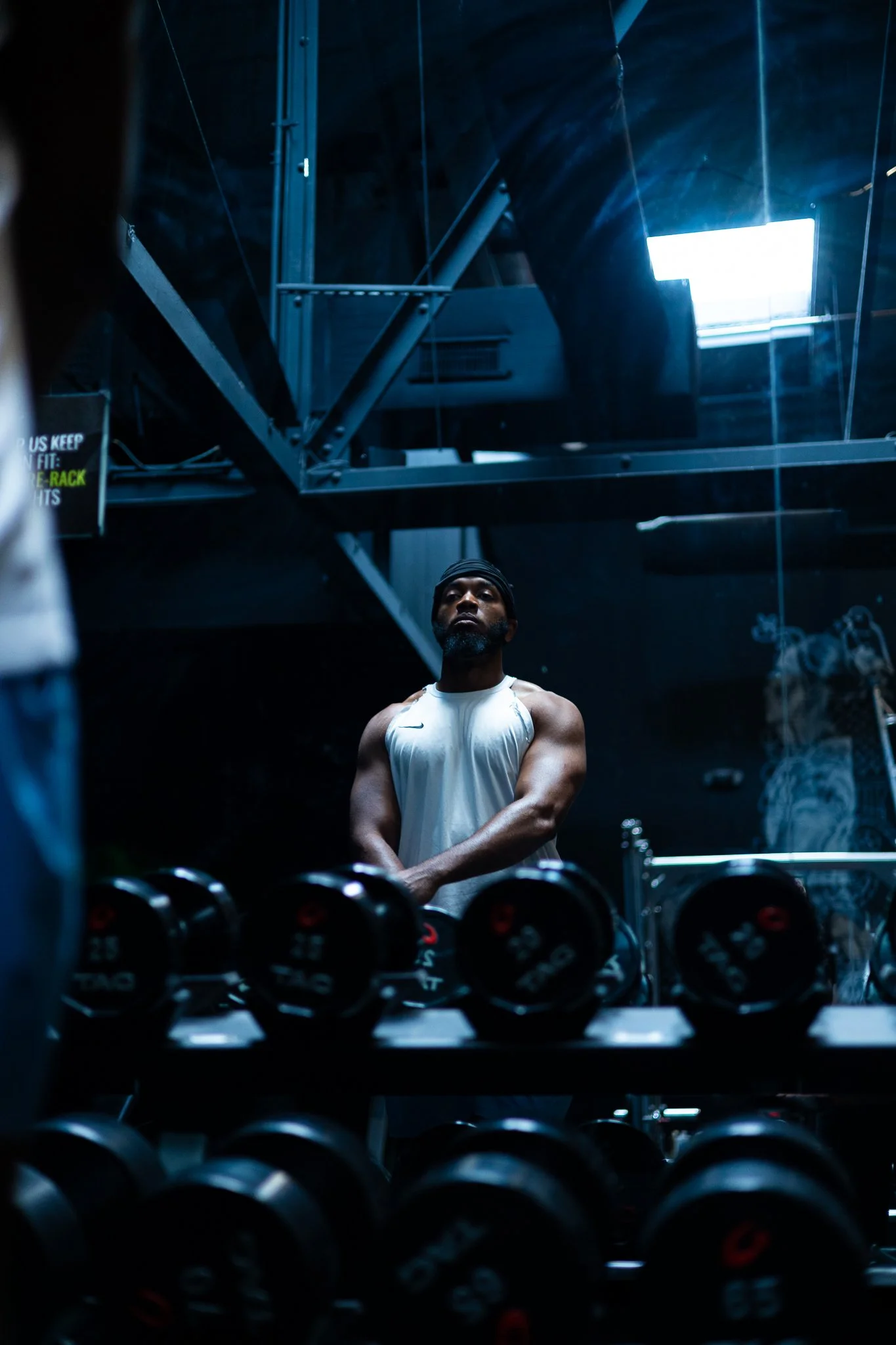 Male muscular athlete standing in front of mirror and dumbbell rack at gym