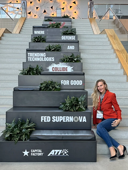 A woman in a red blazer sitting on stairs with black blocks displaying words related to technology and innovation, arranged to spell out a message.
