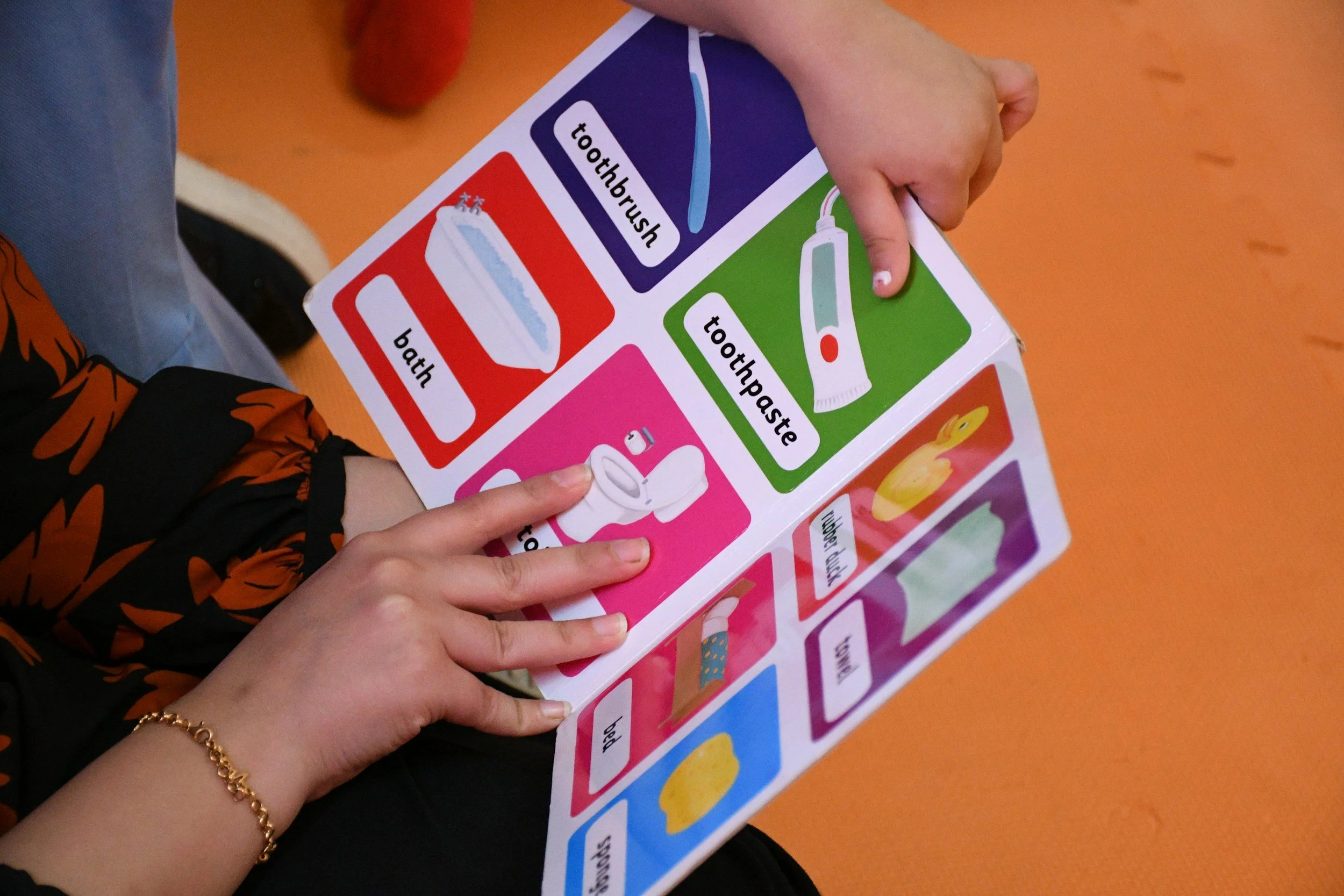 A person holding an educational colorful chart about personal hygiene and health, featuring sections about brushing teeth, bathing, and other hygiene routines.
