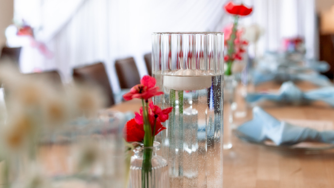 photo of a floating candle, red flowers on a wooden table with blue napkins