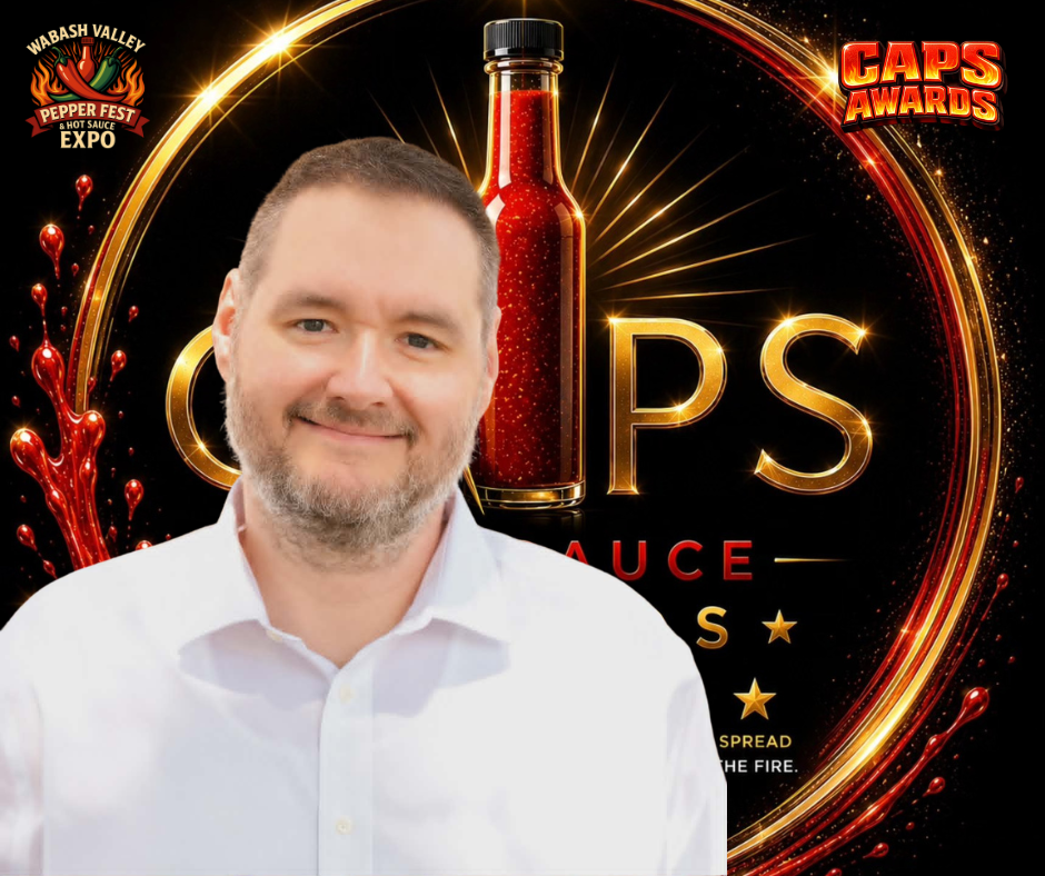 A smiling man with short brown hair and a beard, wearing a white shirt, standing in front of a promotional background for a hot sauce event titled 'Caps Awards.' The background features a large red hot sauce bottle, gold and red glowing accents, and 