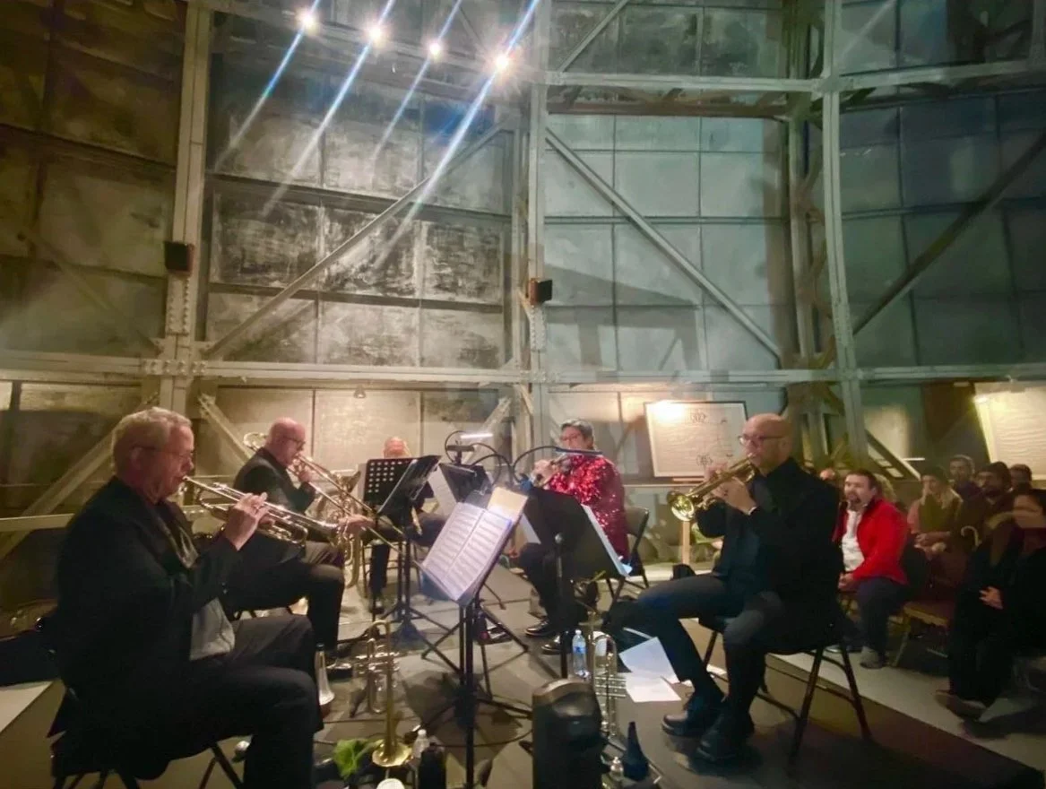 A jazz band performing on stage indoors, with audience members seated and watching.