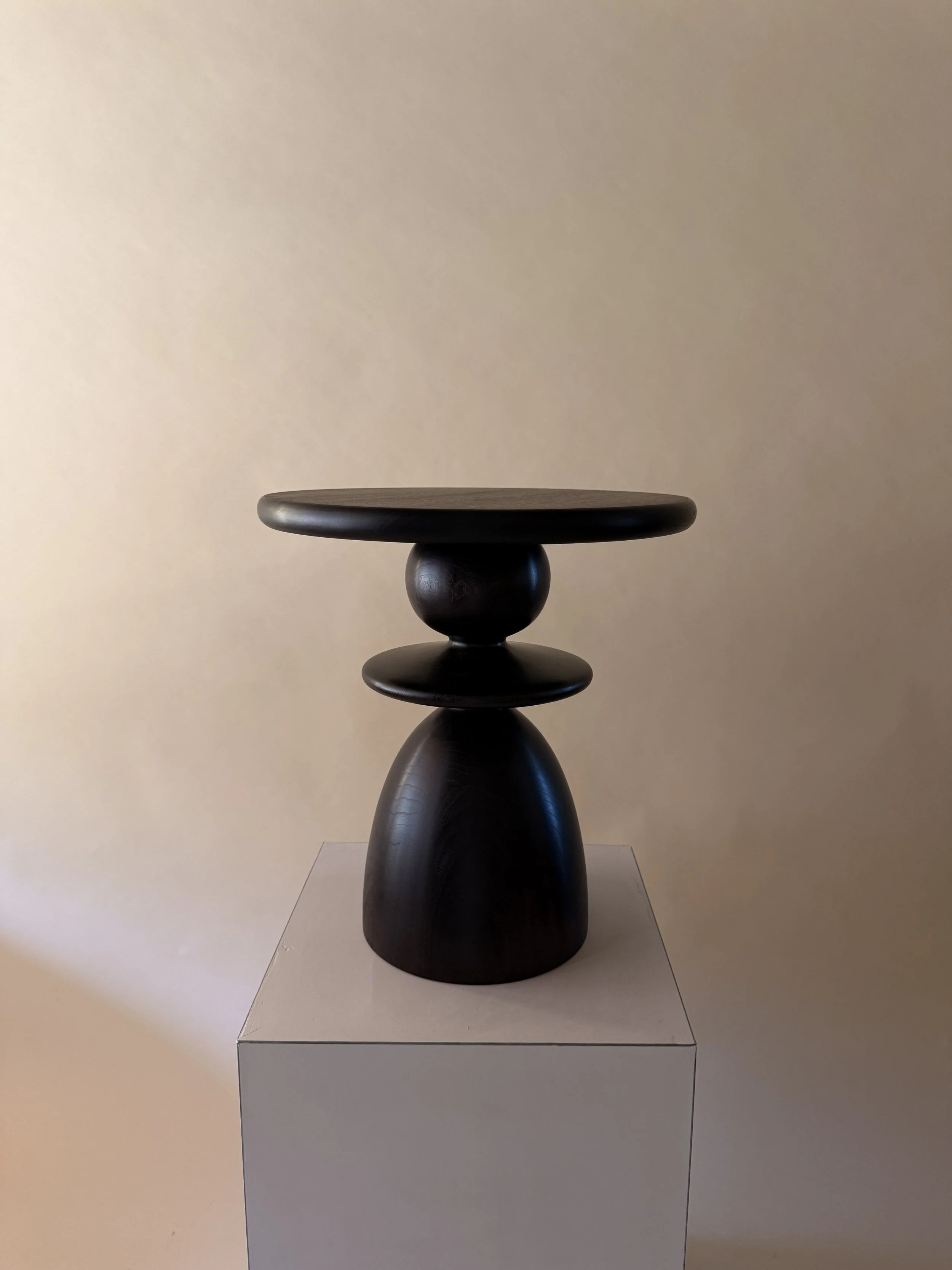 A dark wooden sculpture of an abstract figure on a white pedestal in a gallery.