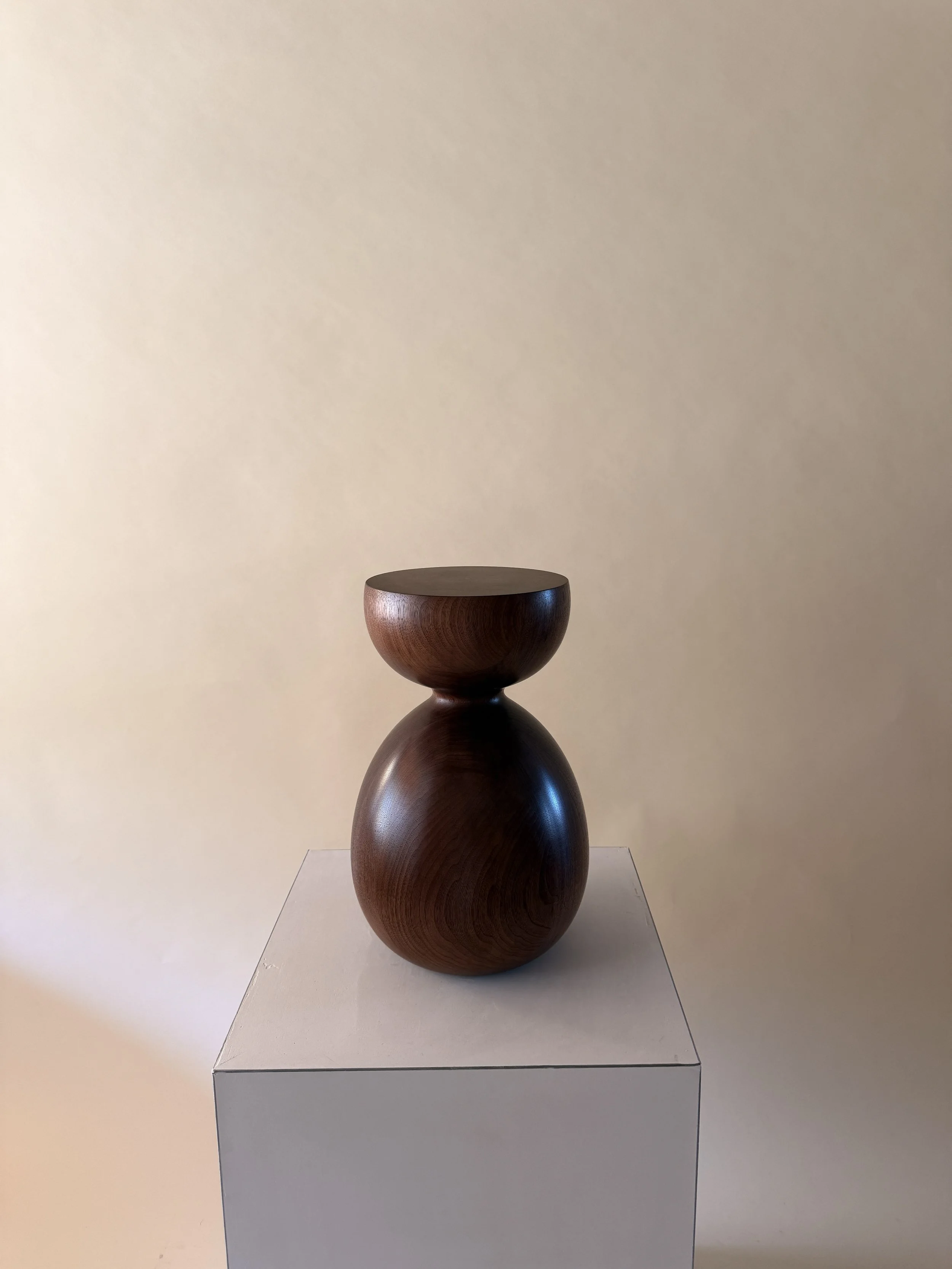 A sculpture of two stacked wooden bowls on a white base against a beige wall.