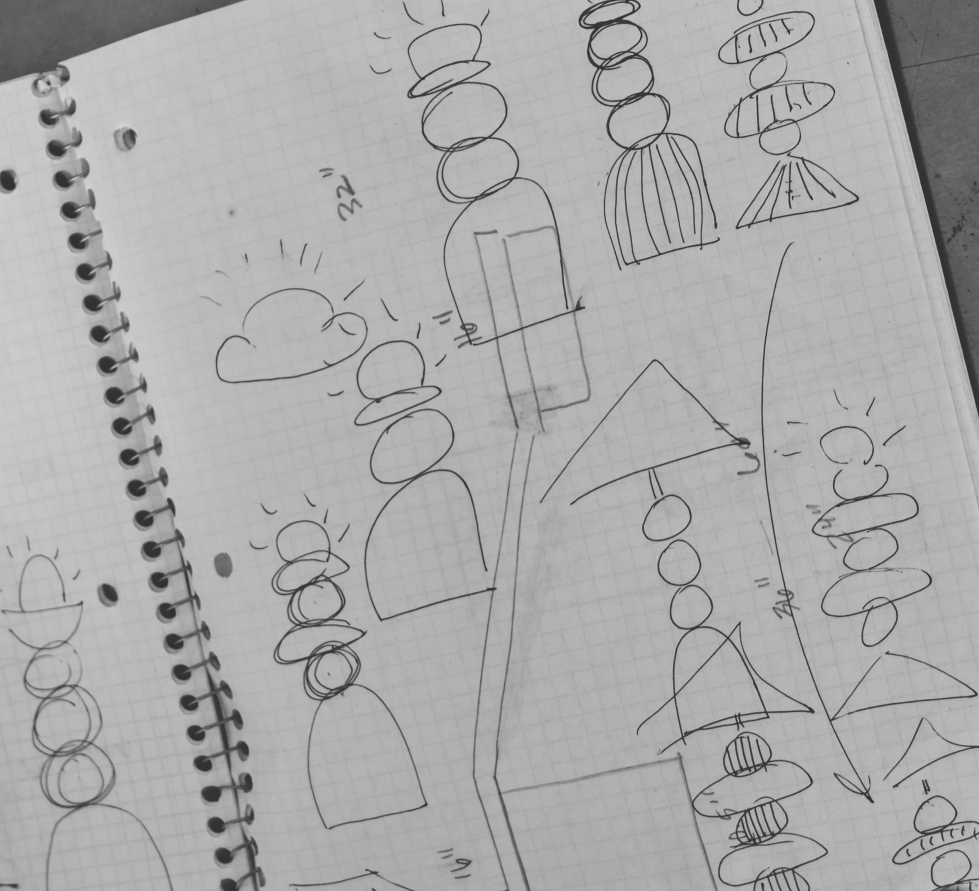 A spiral notebook with handwritten sketches and notes, including diagrams, stick figures, and symbols, on graph paper.