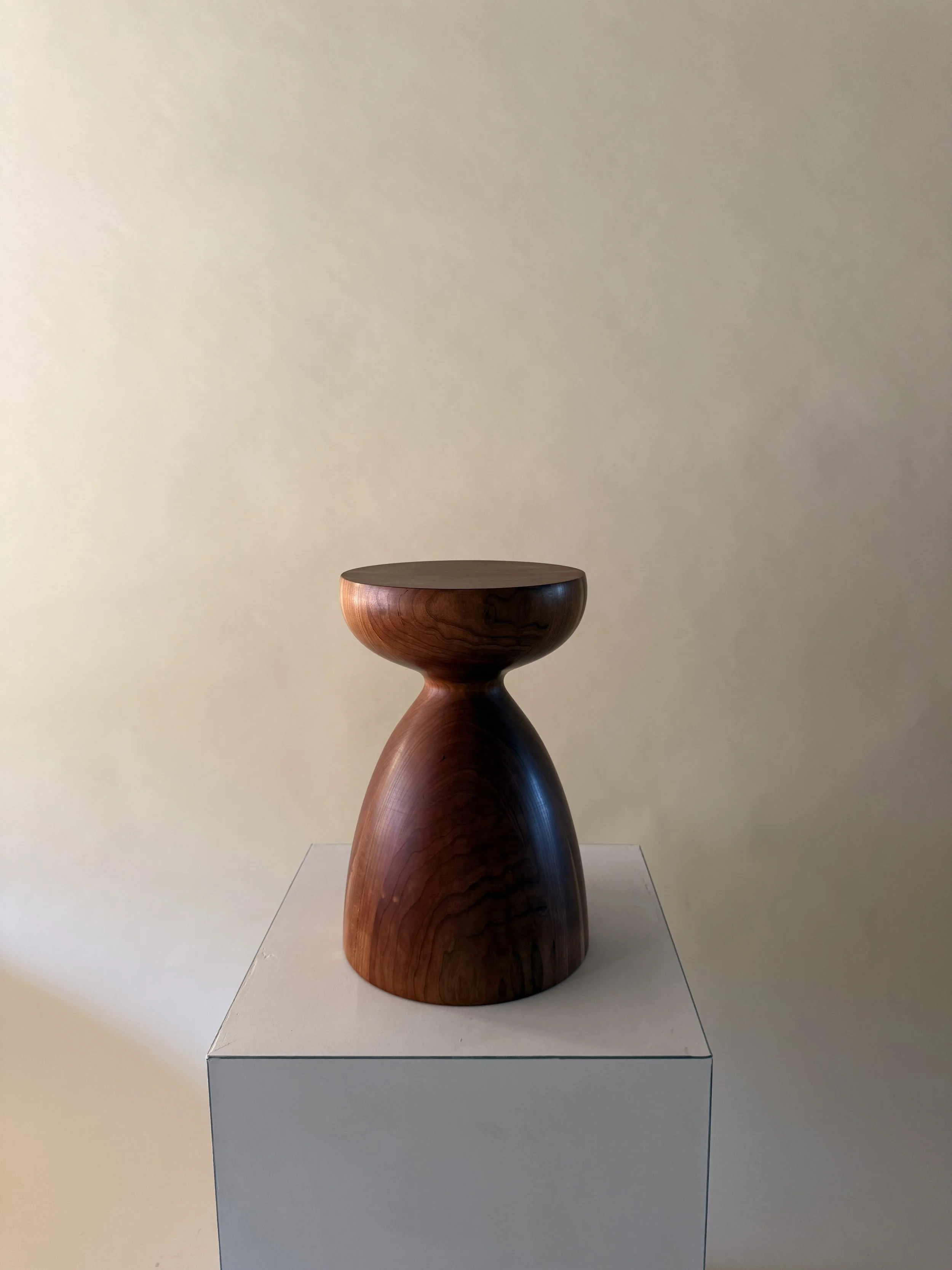 Wooden sculpture on a white pedestal against a beige wall.