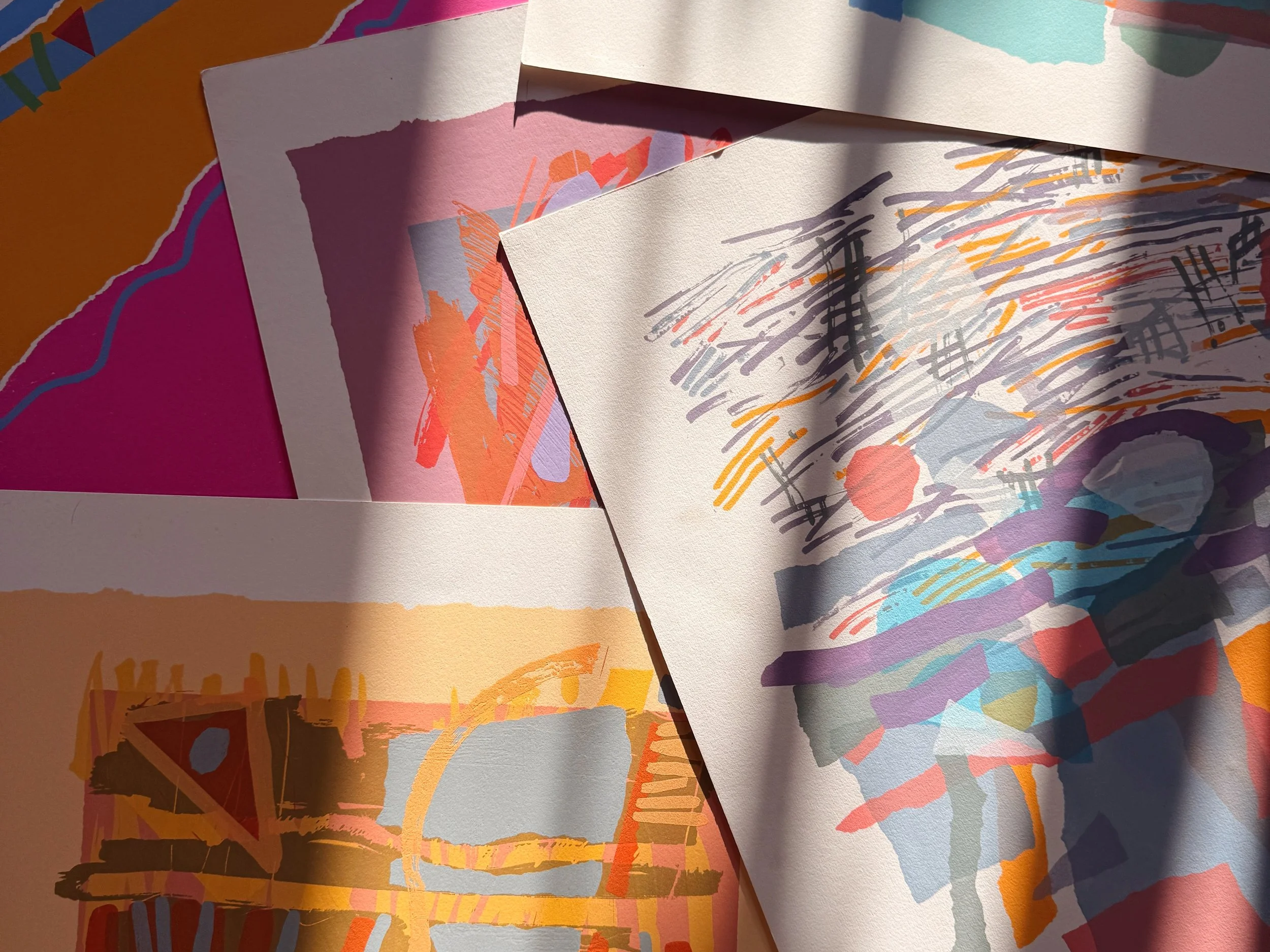 Various colorful abstract watercolor paintings or prints layered over each other on paper.