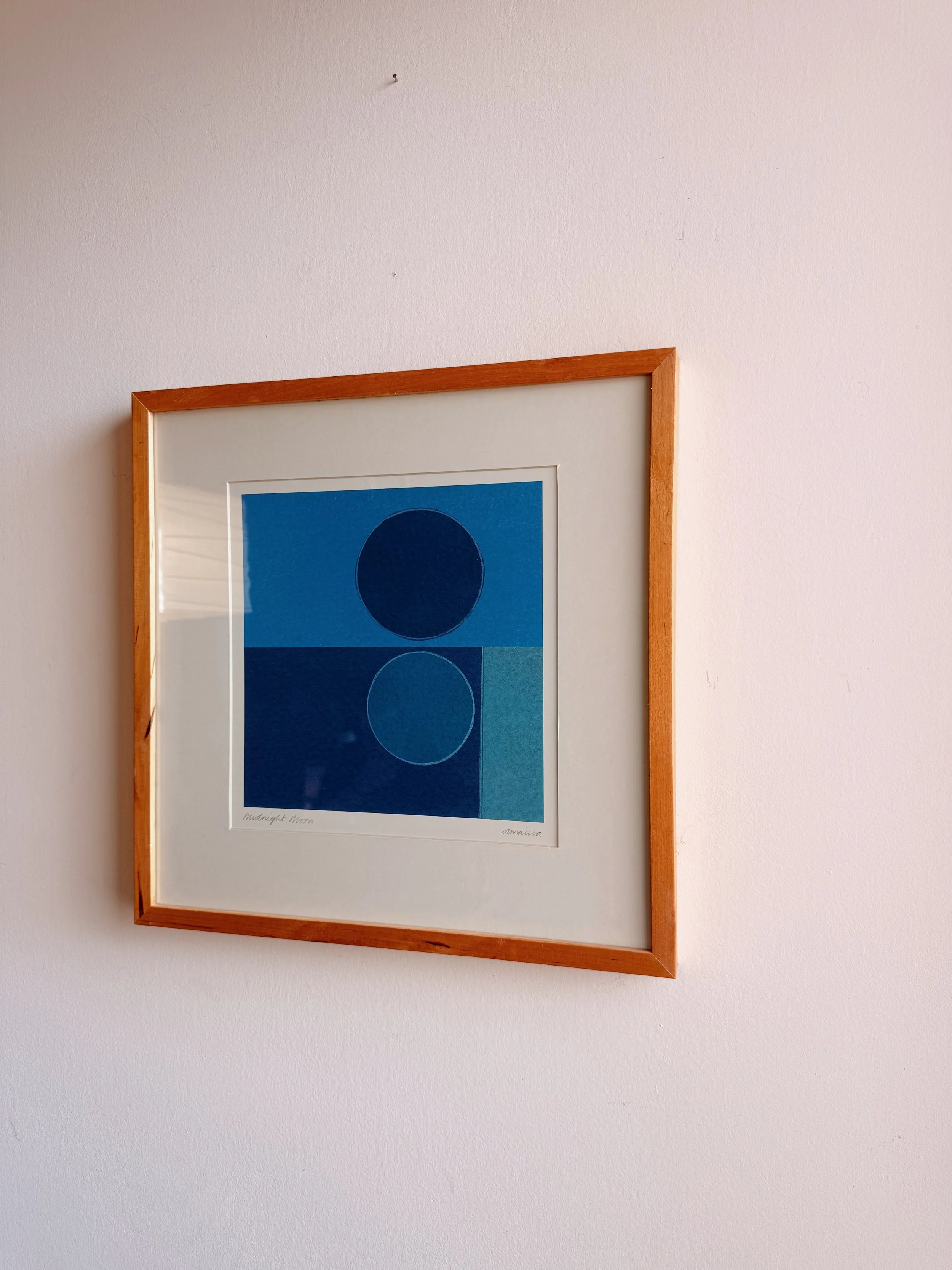 A framed print of a blue abstract artwork with three circles in different shades of blue, mounted on a white wall.
