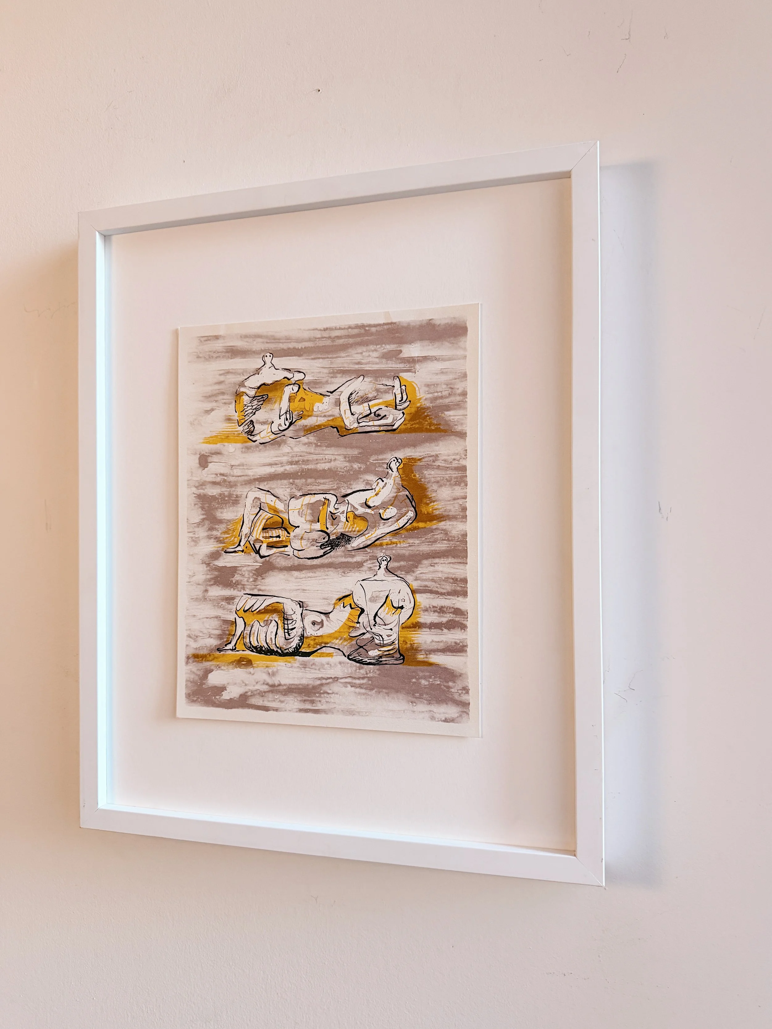 Framed abstract artwork featuring line drawings of reclining, prone, and seated figures in neutral tones with yellow highlights, mounted on a wall.