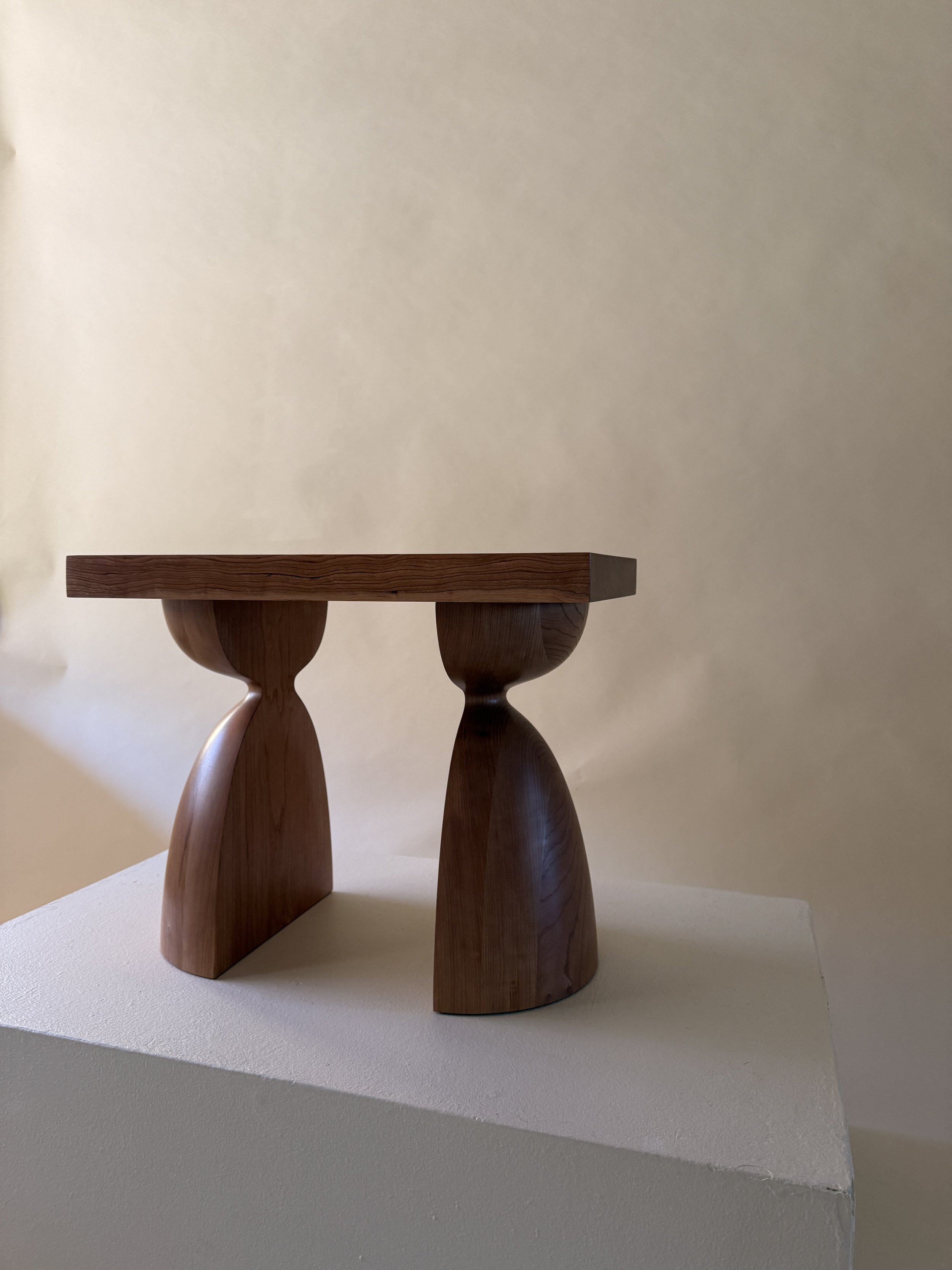 A wooden table with a flat rectangular top and rounded legs on a white surface, against a beige wall.
