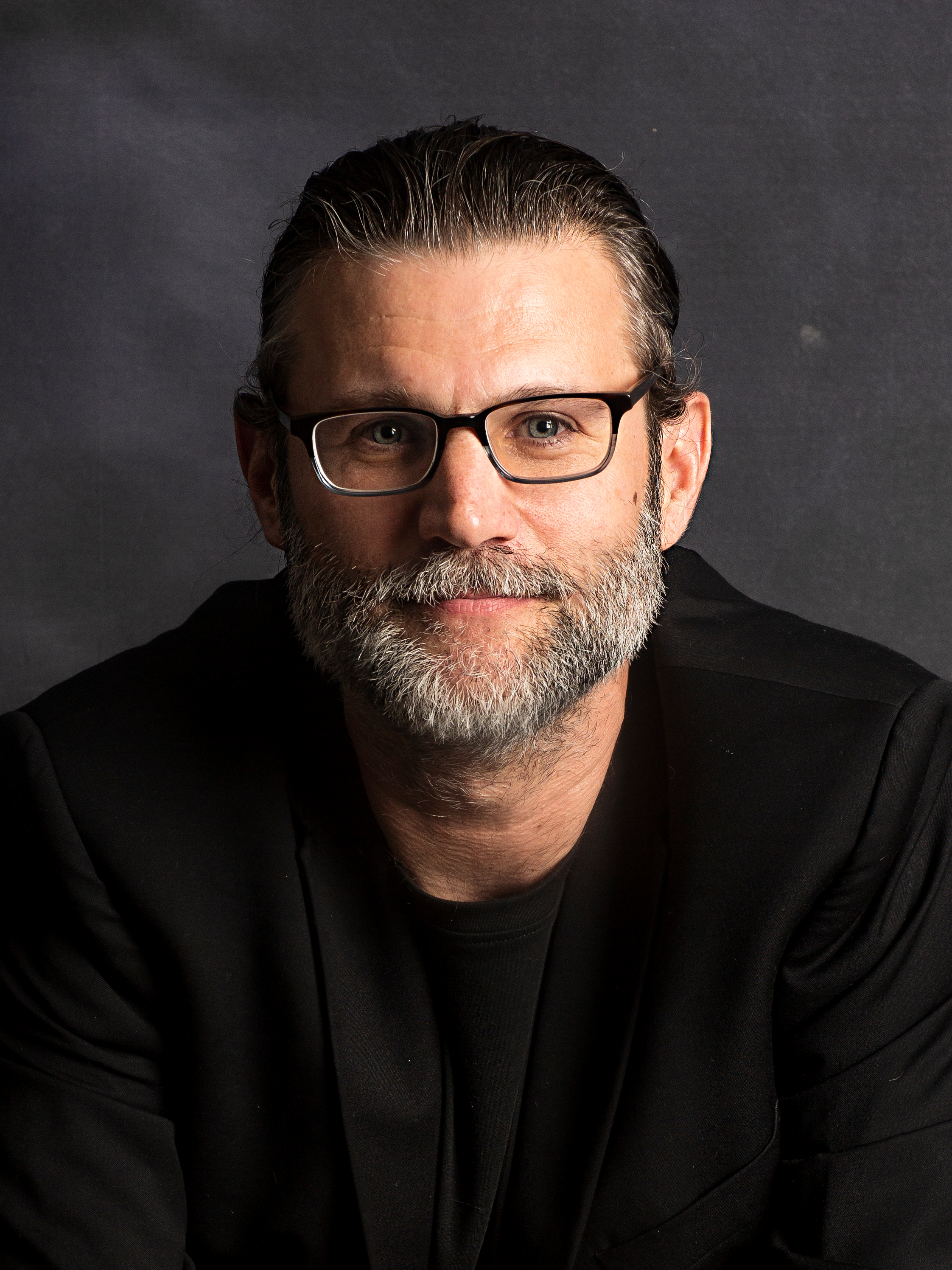 Man with black glasses, brown hair pulled back ad a grew beard.
