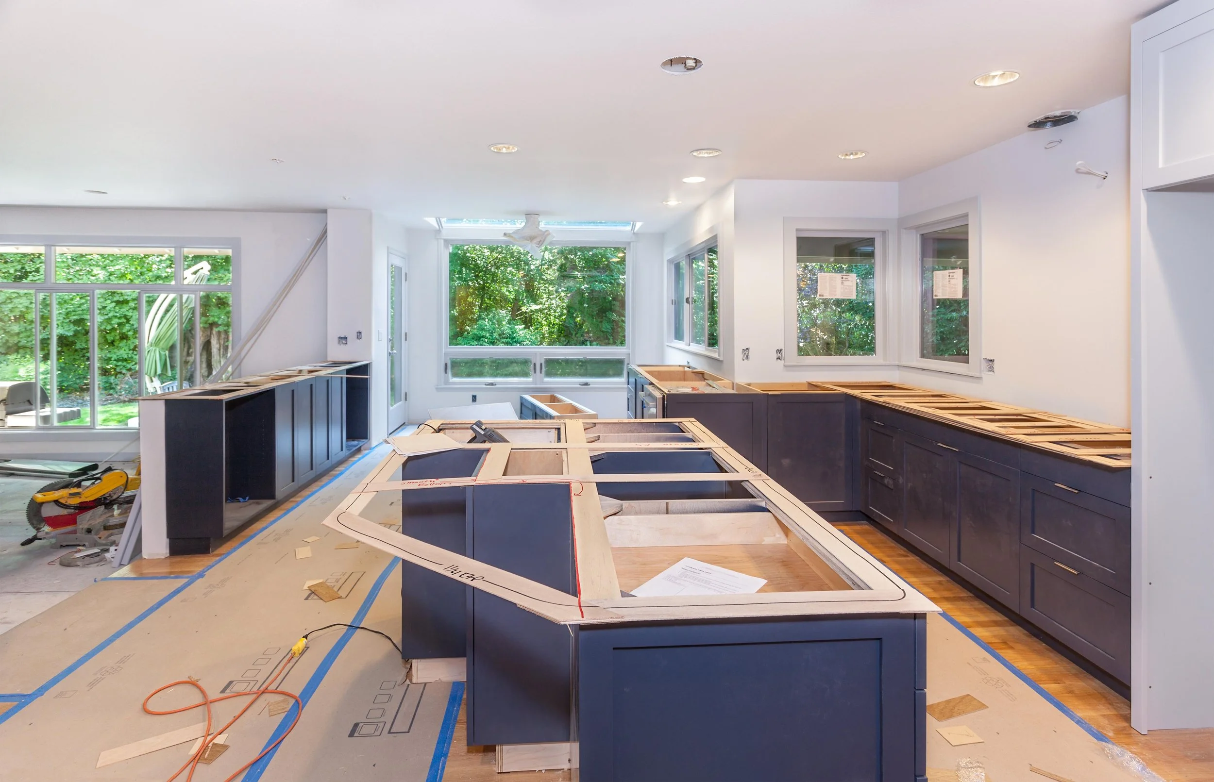 Kitchen under construction with dark blue cabinets, wooden countertops, large windows, and construction tools and materials scattered around.
