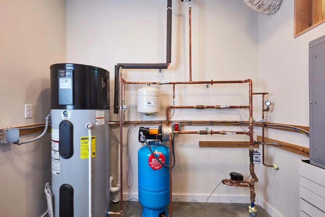 A utility room with a water heater, pressure tank, and copper pipes for plumbing.