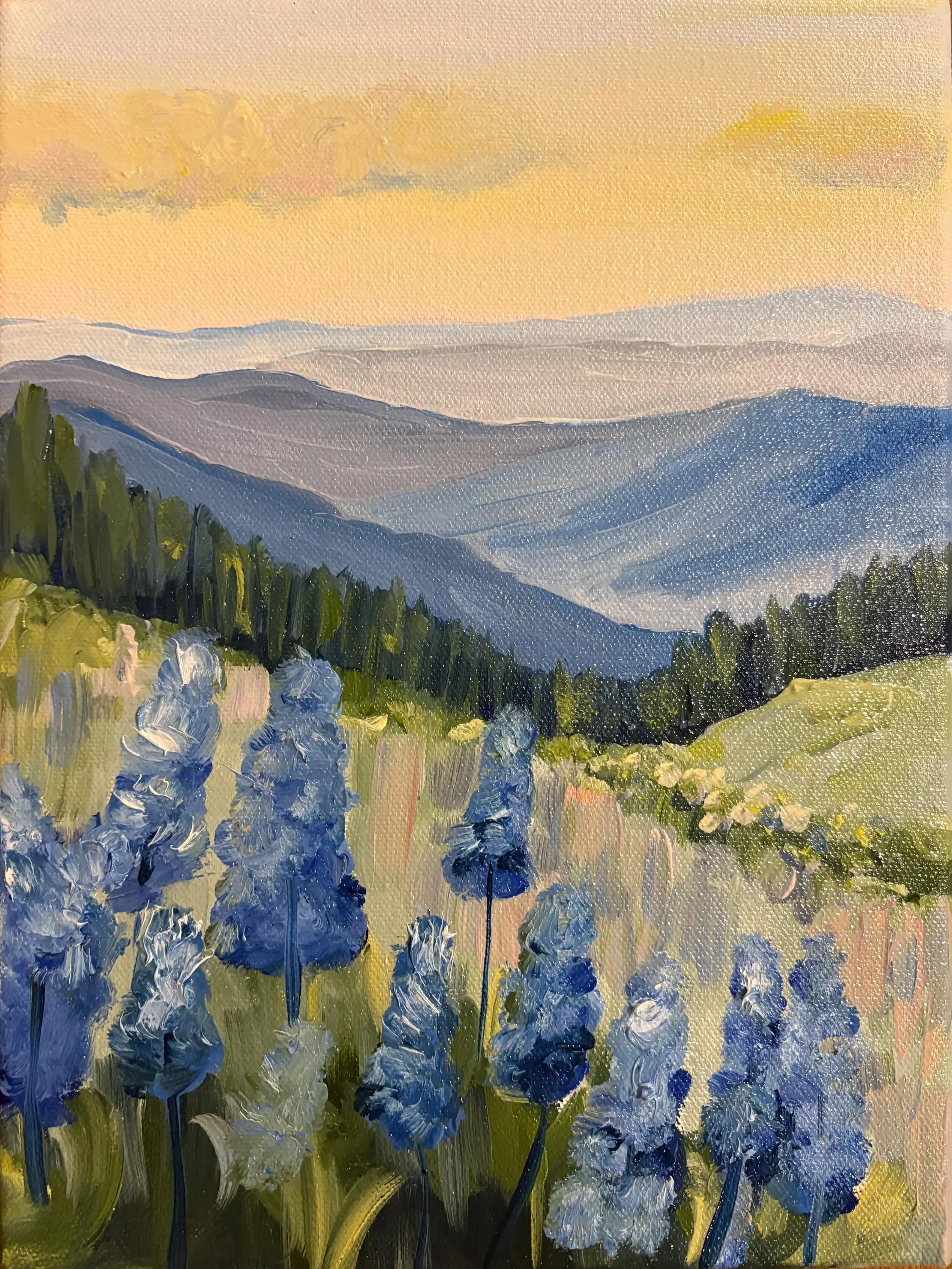 Oil painting of a mountain landscape at sunset, with blue and purple peaks, green foreground, and a yellow-orange sky with soft clouds.