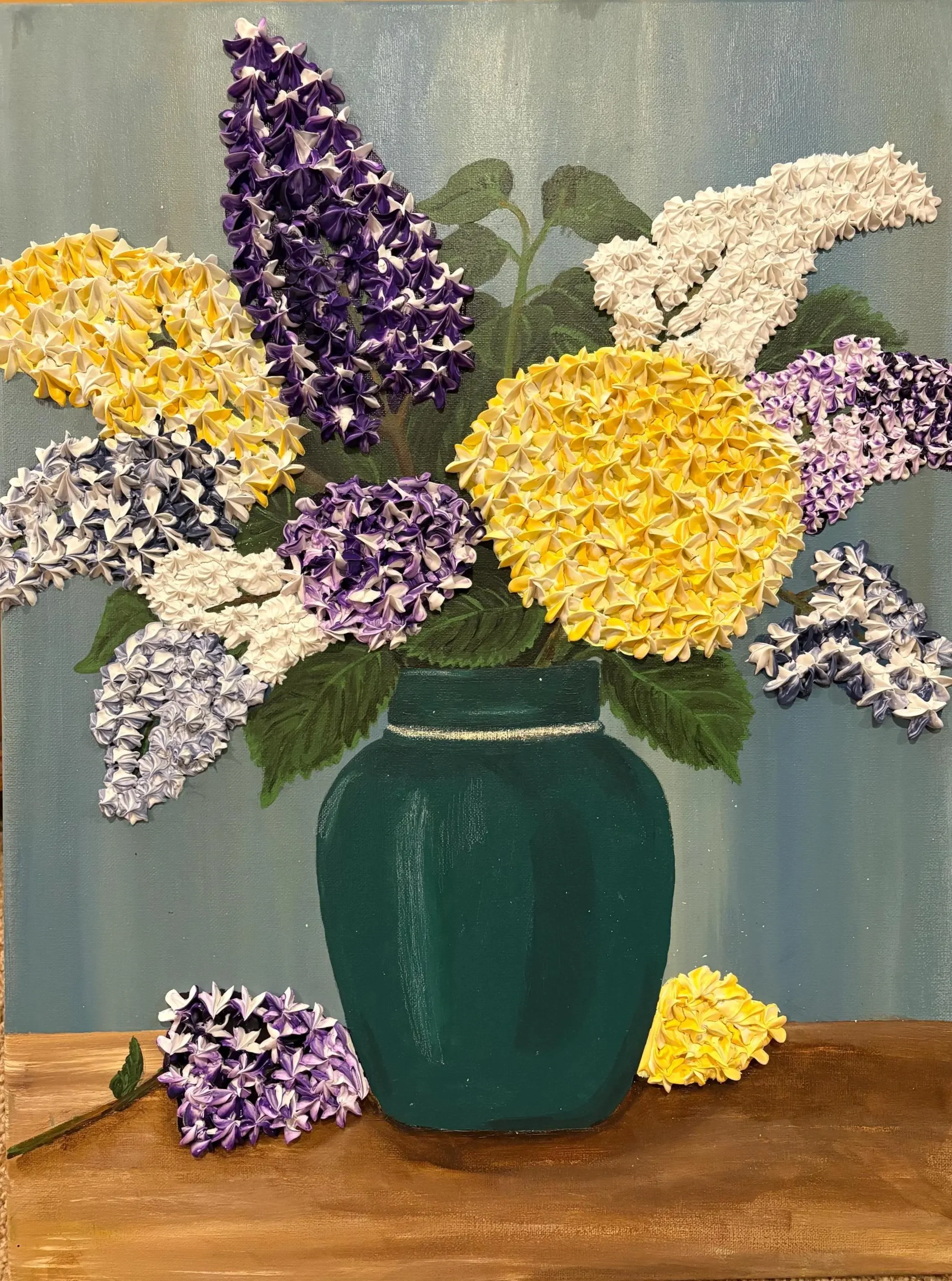 A painting of a green vase filled with purple, yellow, white, and lavender hydrangea flowers, with some flowers laying on a wooden surface.