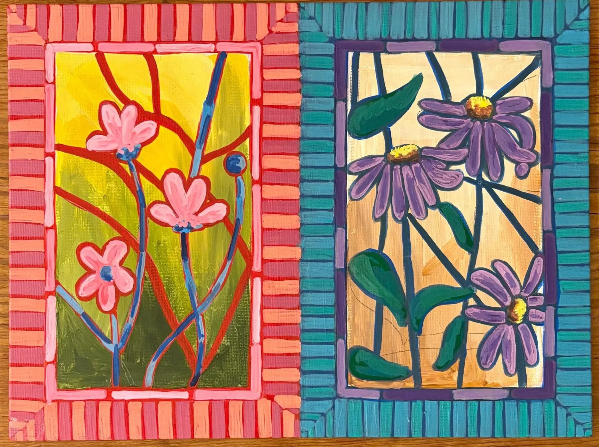 Two colorful paintings side by side, each featuring floral designs with outlined flowers and leaves, set within striped borders on a wooden surface.