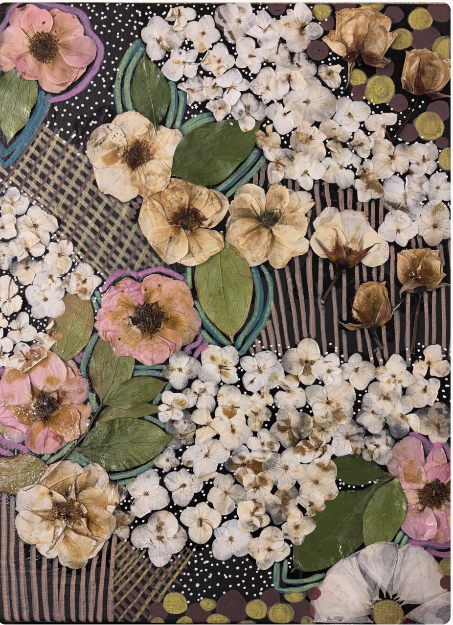 An art piece made of pressed flowers, leaves, and small decorative elements arranged on a black background with colorful stitching and dotted patterns.