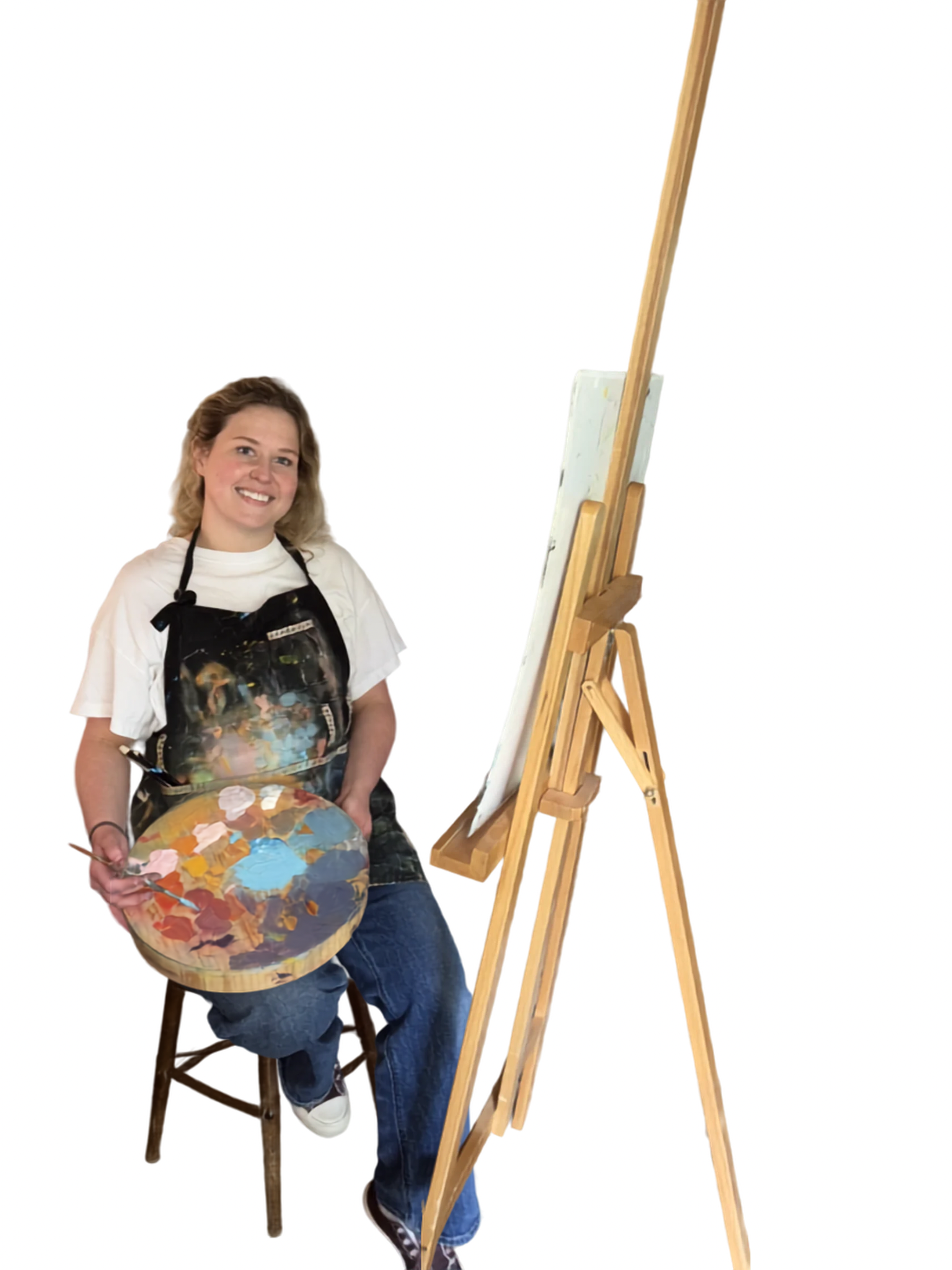 A woman sitting on a wooden stool, holding a paint palette and brush, in front of an easel with a blank canvas, ready to paint.
